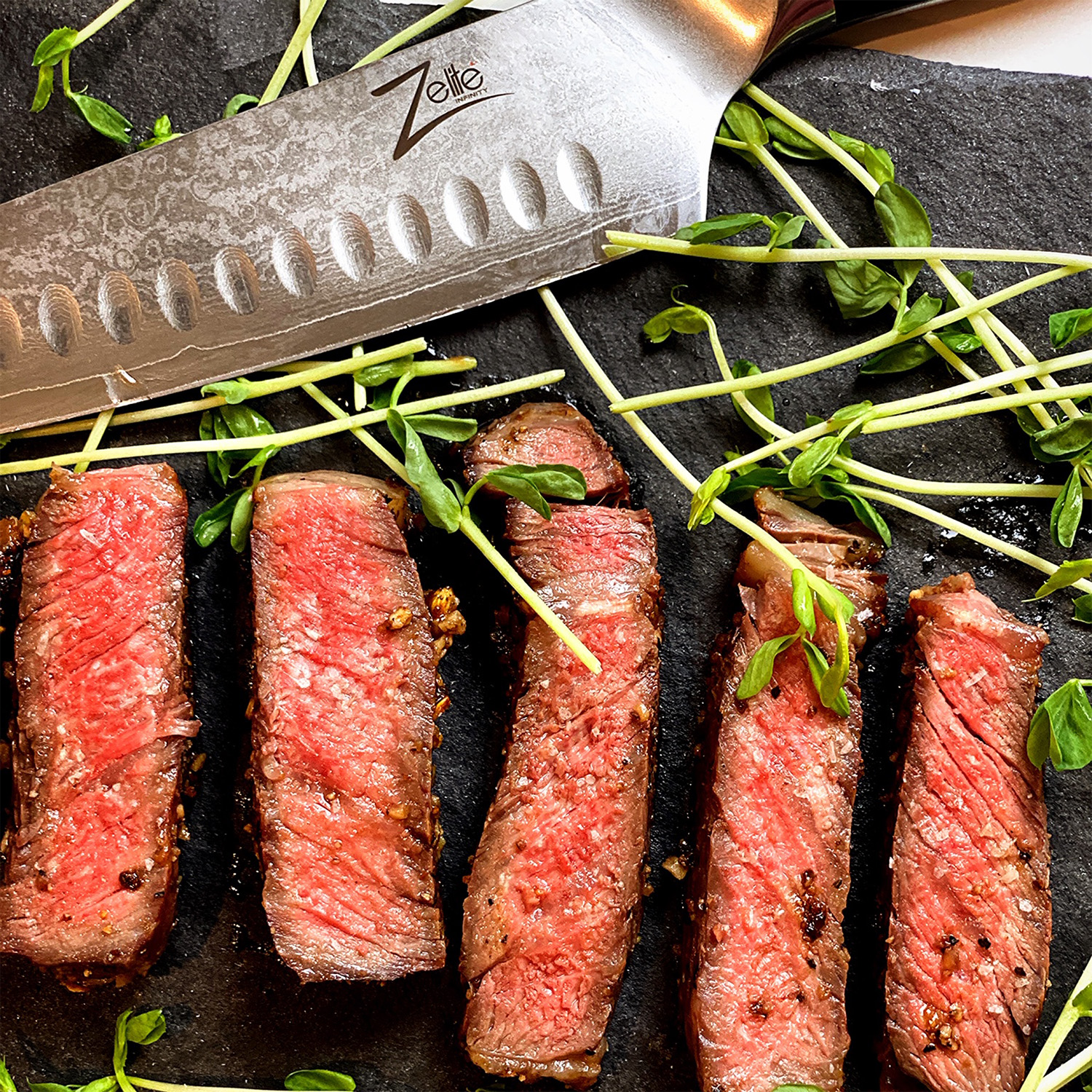 Scheiben gebratenes Steak mit einem Messer. Grüne Sprossen auf schwarzer Steinoberfläche.