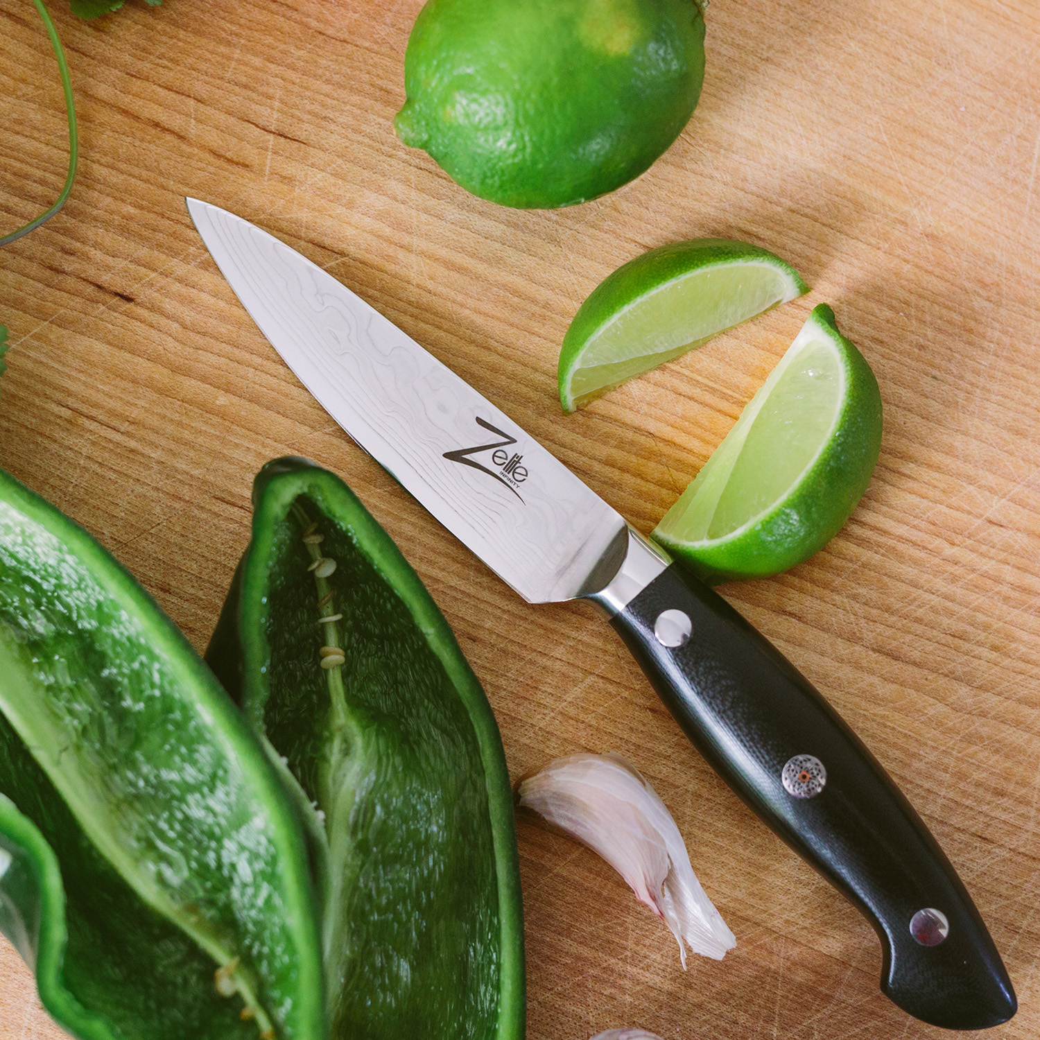 Ein Kochmesser mit schwarzem Griff, neben Limetten und einer Knoblauchzehe auf einer Holzoberfläche.