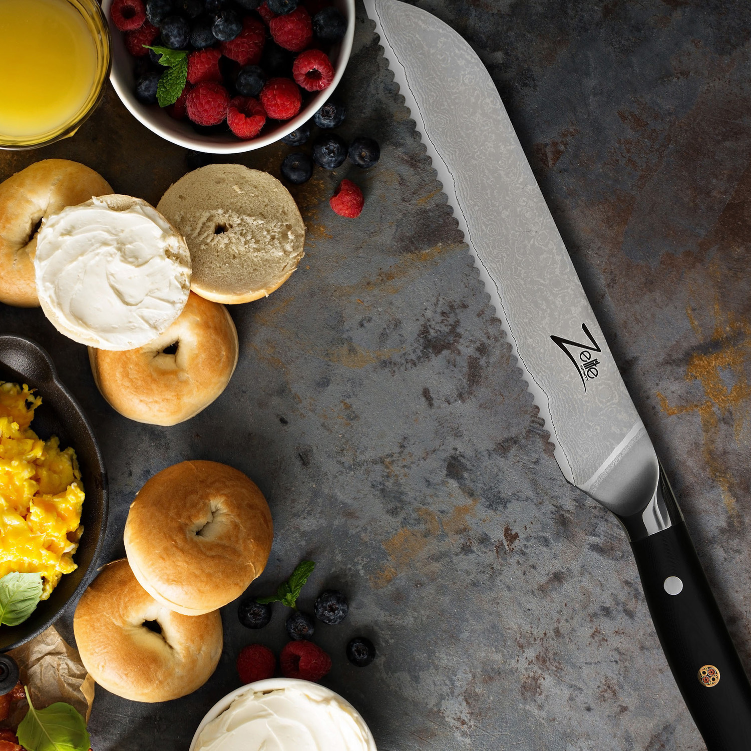 Bagels mit Frischkäse, Beeren und einem gezahnten Messer auf einer strukturierten Oberfläche.