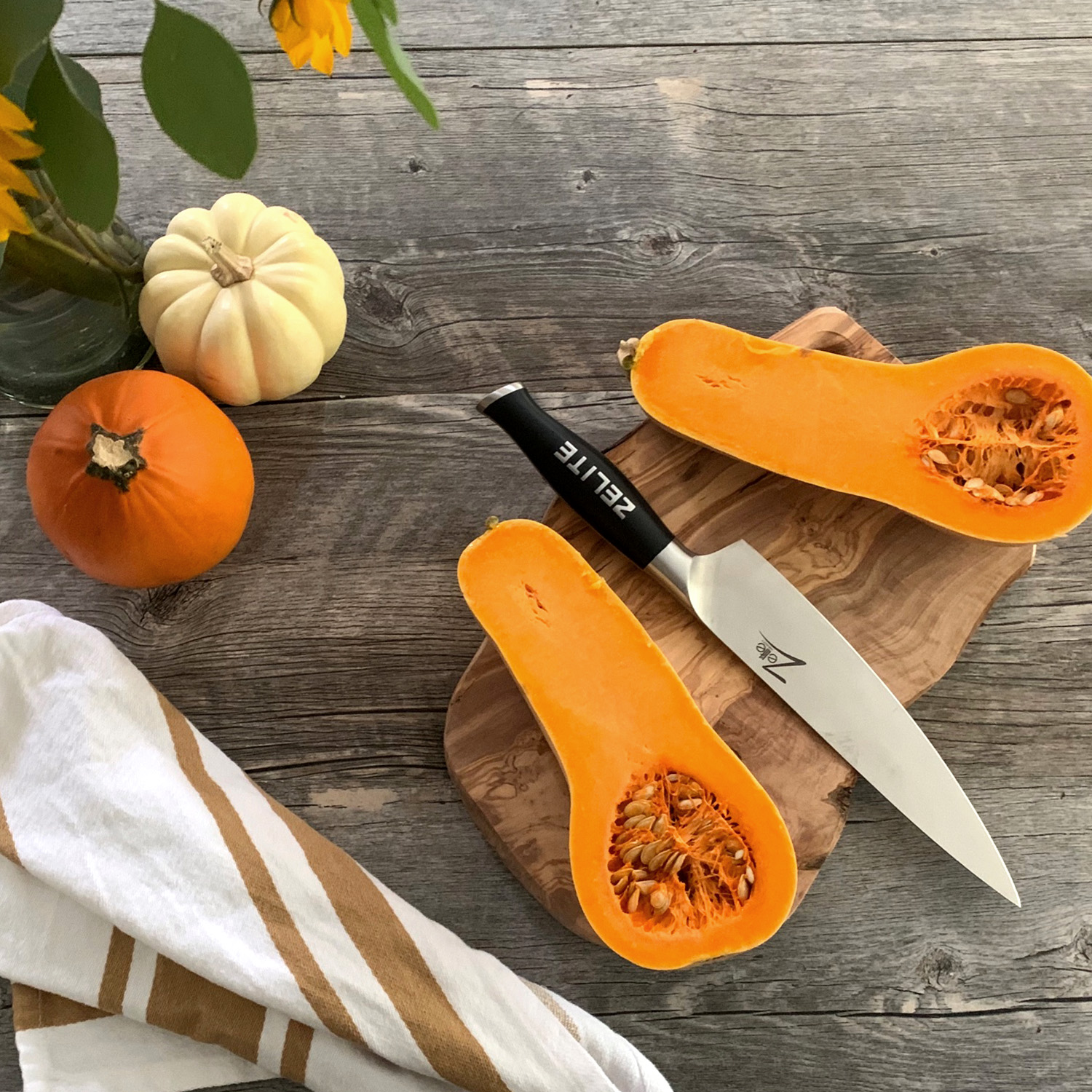 Butternusskürbishälften, ein Messer, Kürbisse und ein Handtuch auf einer Holzoberfläche.