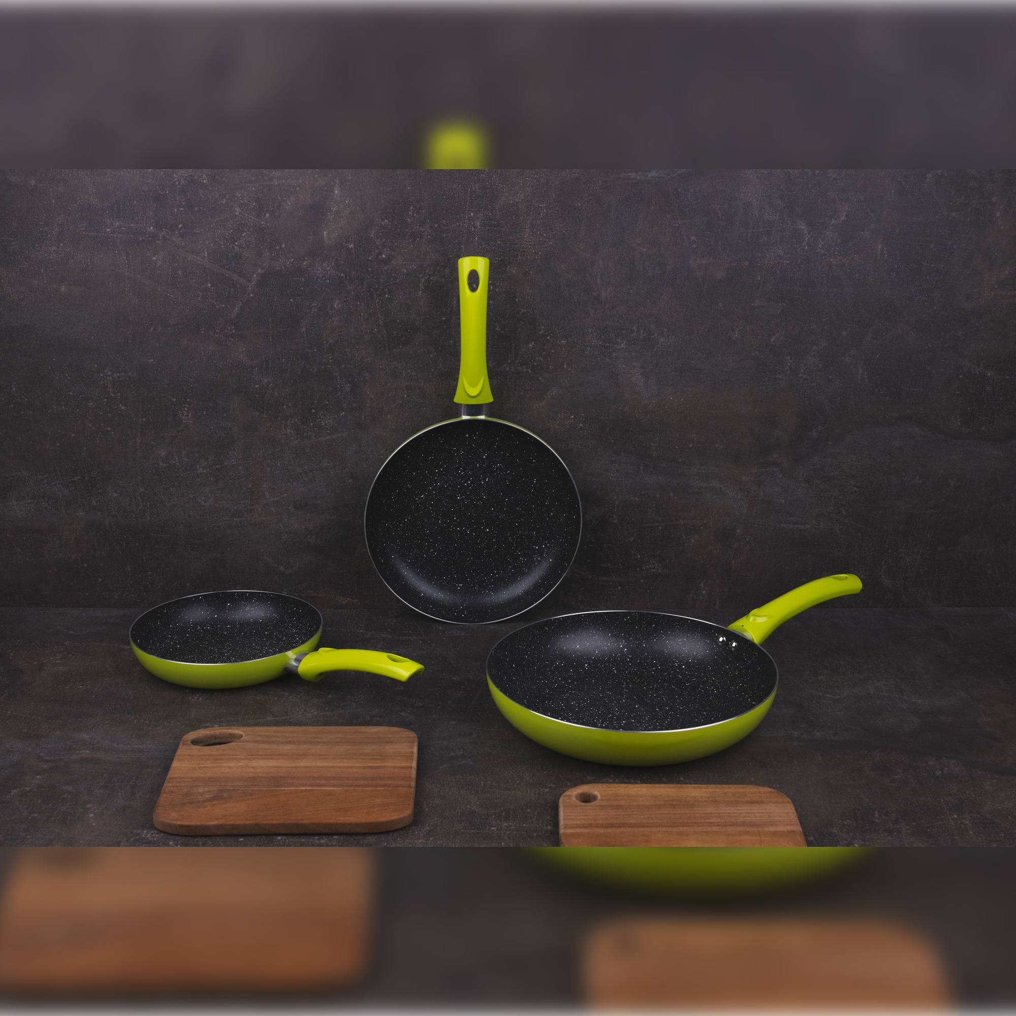 Cuatro sartenes con mangos verdes, superficie negra. Dos tablas de cortar de madera.