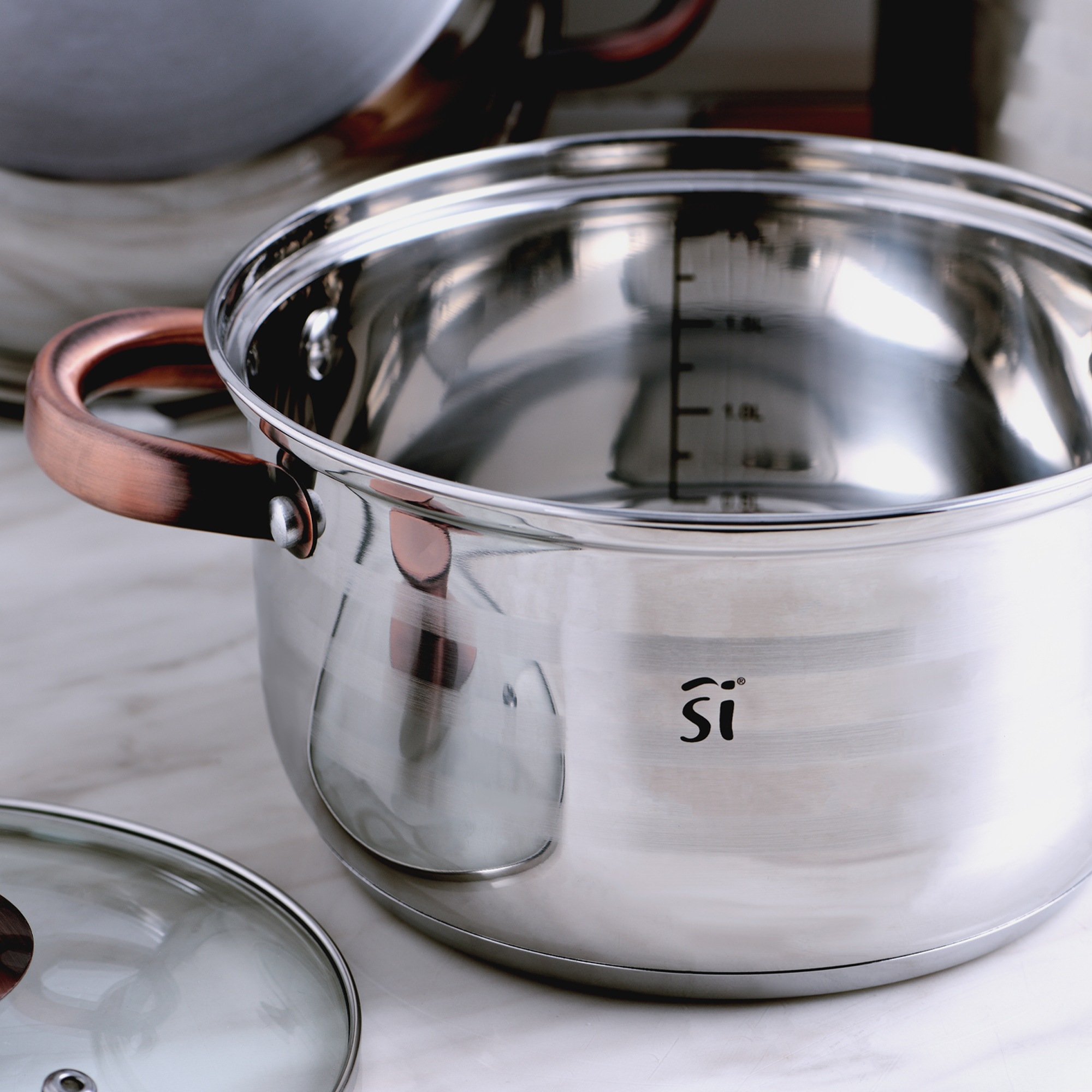 Olla de acero inoxidable con asa de cobre y tapa de vidrio sobre mármol.