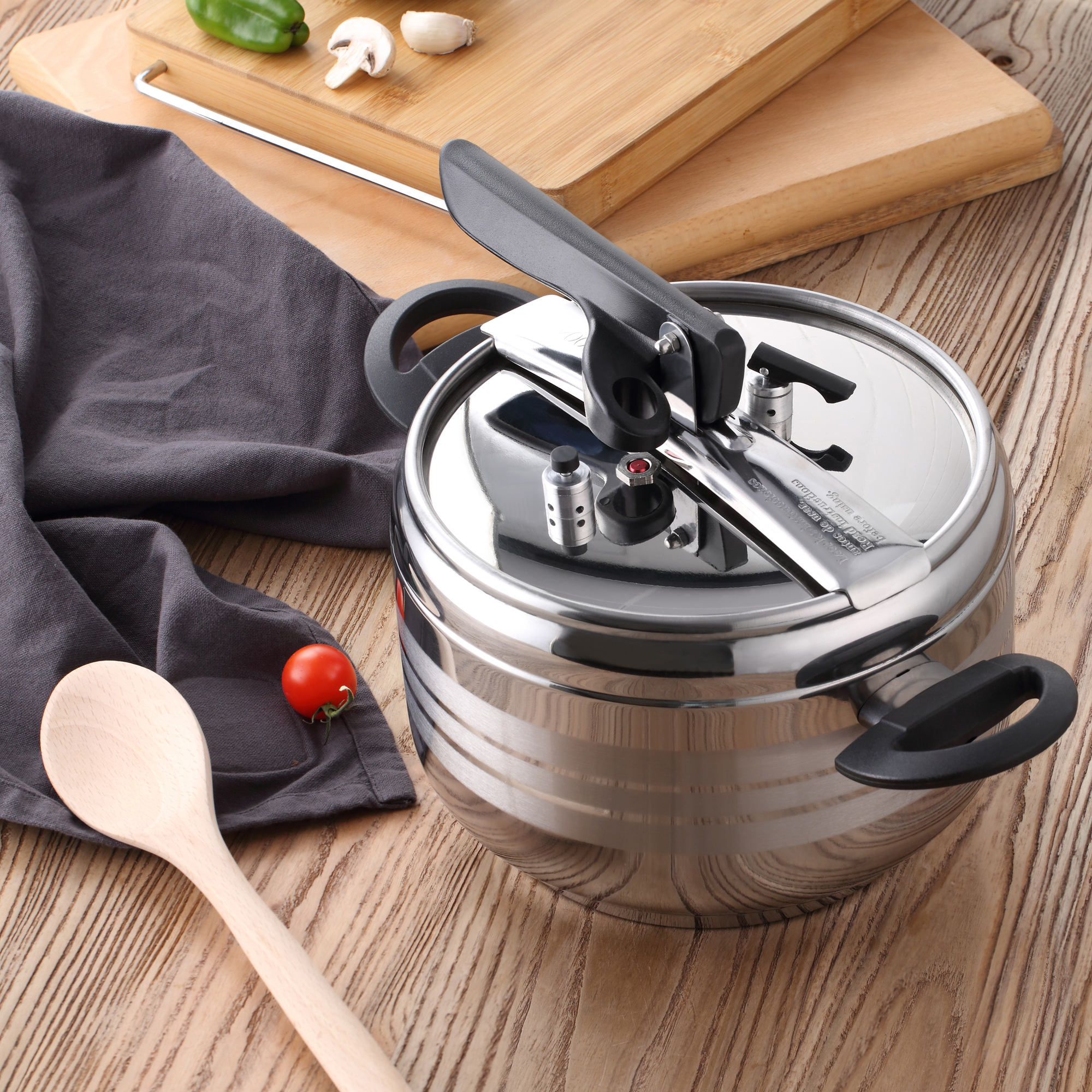 Olla a presión de acero inoxidable con cuchara de madera, tomate e ingredientes sobre madera.