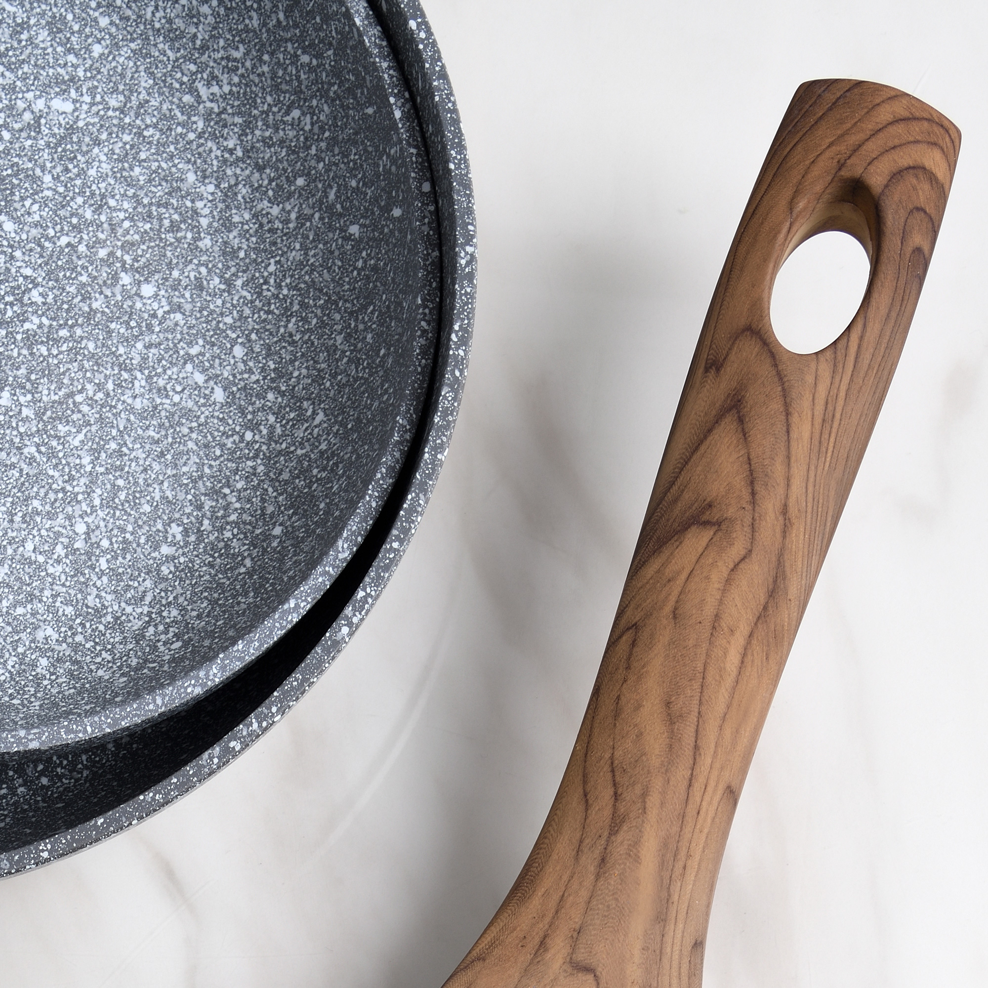 Primer plano de una sartén con mango de madera sobre una superficie de mármol.