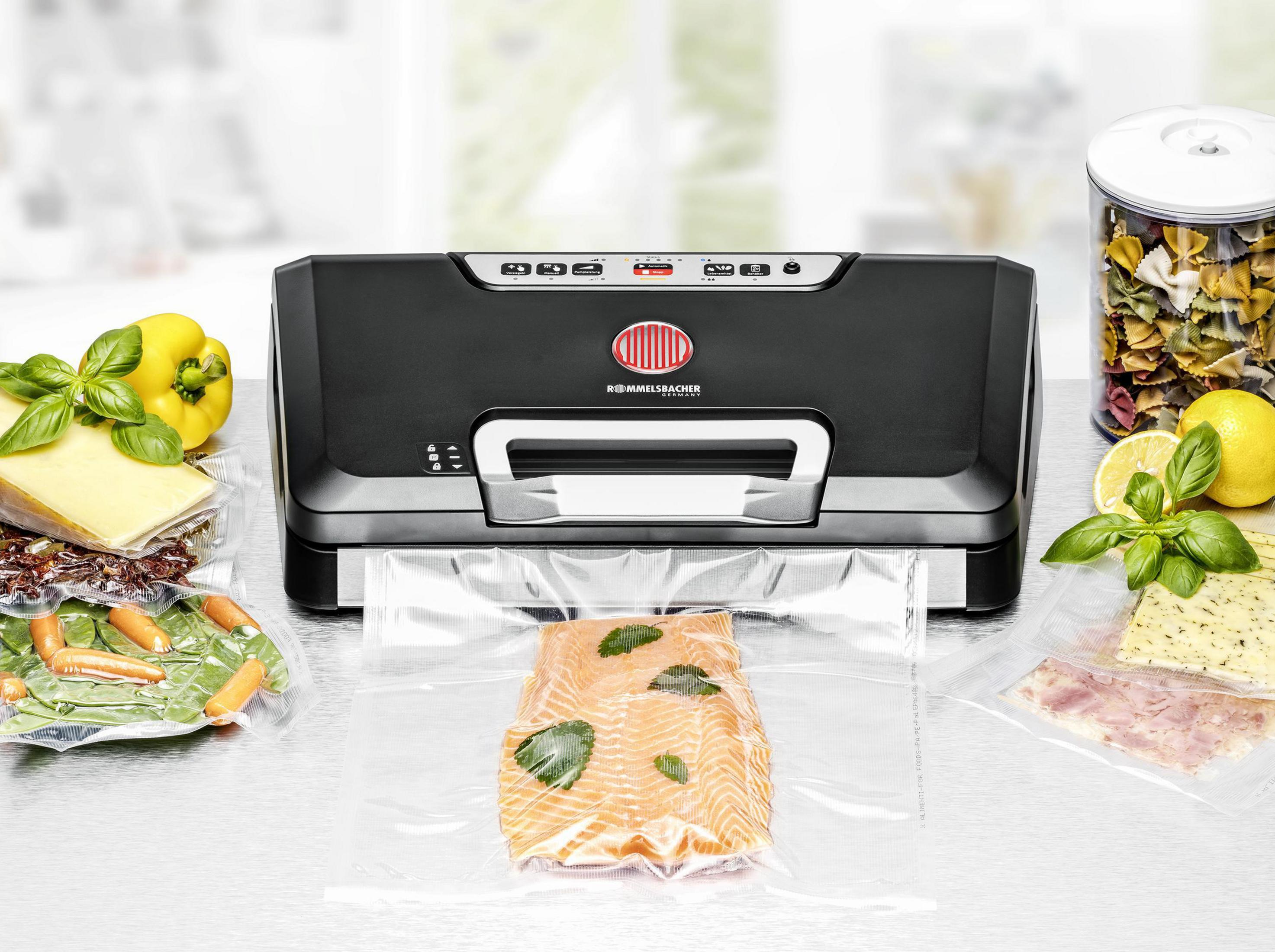 Czarna zgrzewarka próżniowa z produktami spożywczymi w przezroczystych workach. Zawiera łososia, ser i makaron.