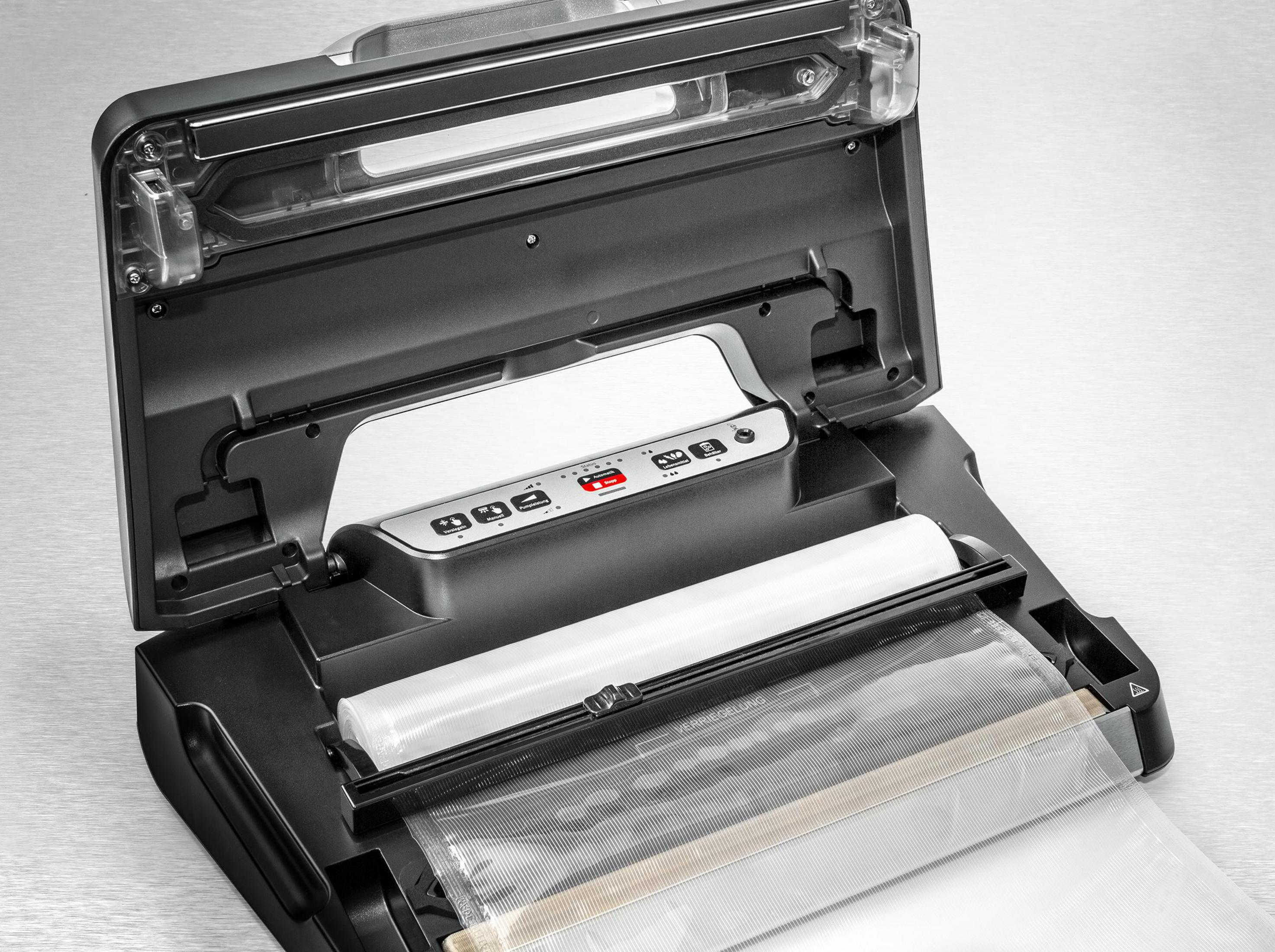 Czarna i szara zgrzewarka próżniowa jest otwarta, z rolką plastiku i widocznymi przyciskami.