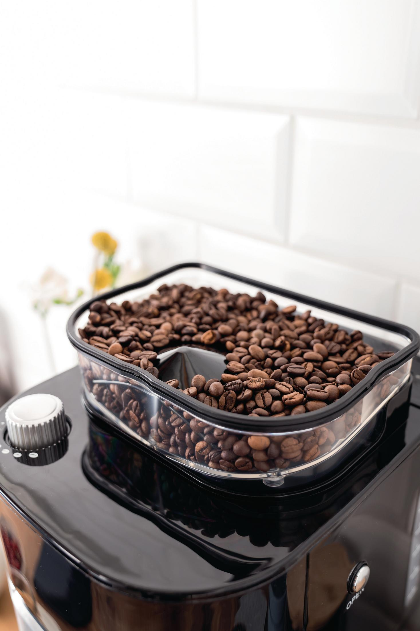 Ziarna kawy w przezroczystym pojemniku na czarnym ekspresie do kawy.