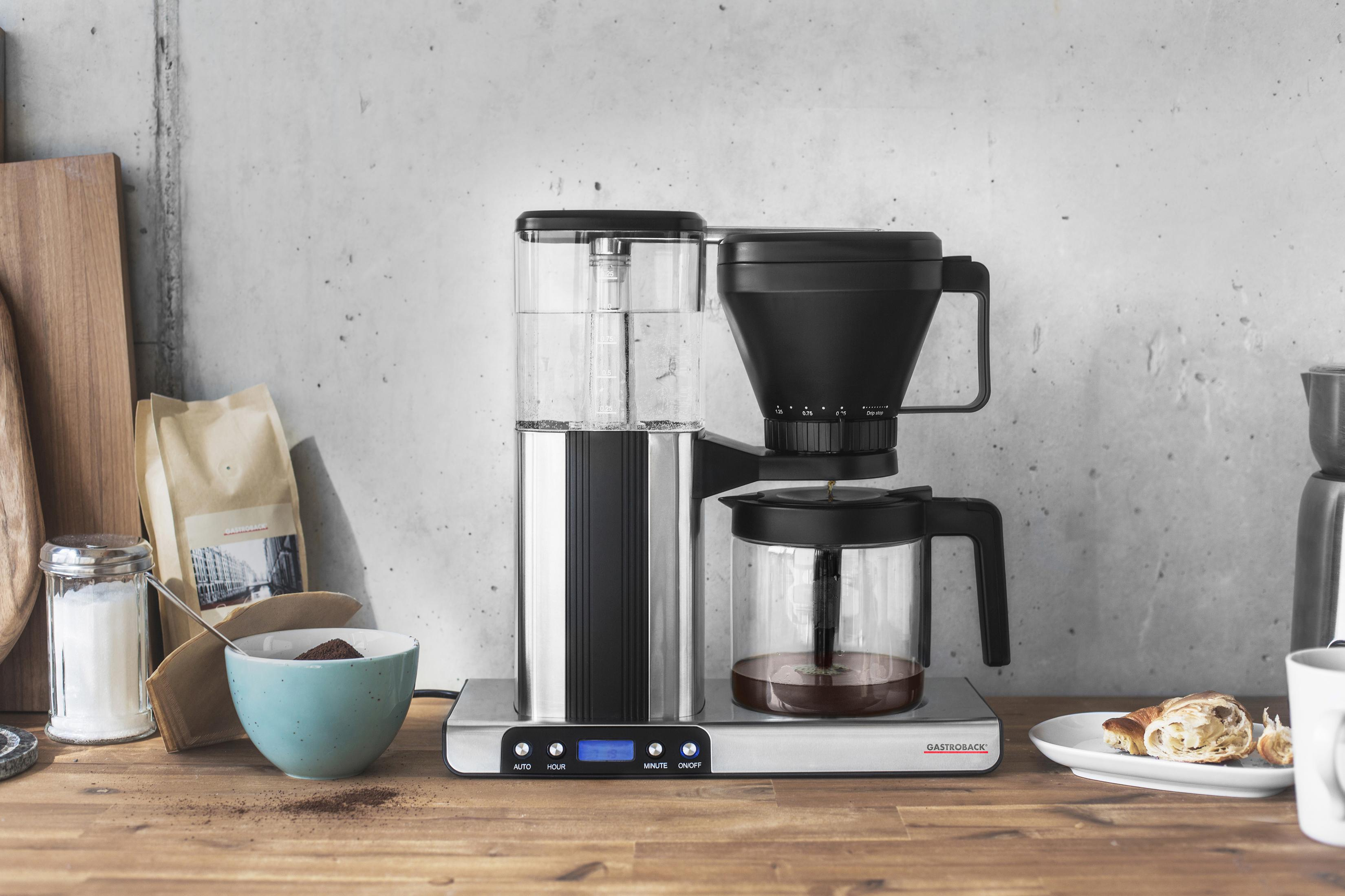 Ekspres do kawy na drewnianym blacie, z kawą mieloną w misce i rogalikiem.