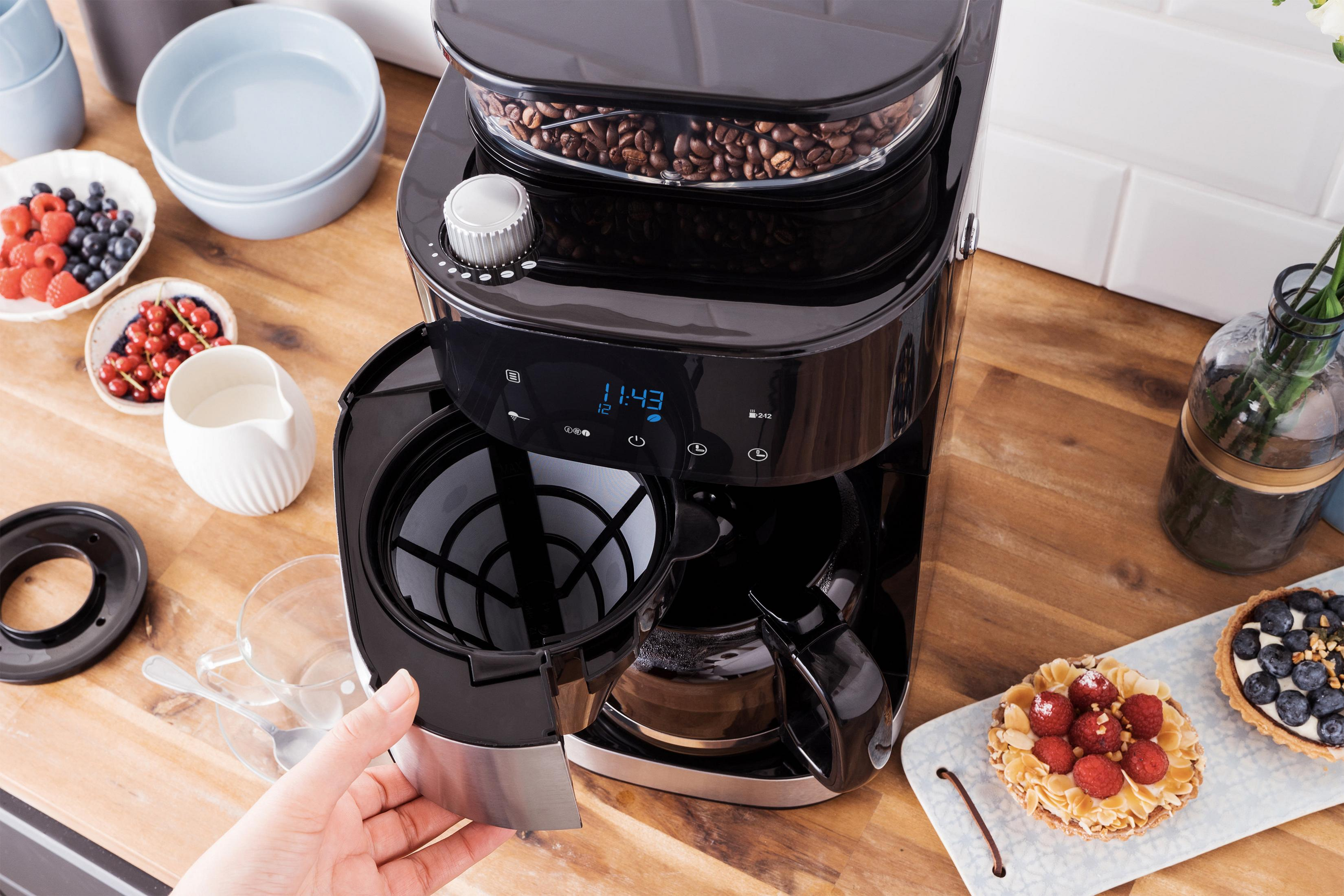 Macchina da caffè con chicchi, tazze e pasticcini su un tavolo di legno, una mano rimuove il filtro.