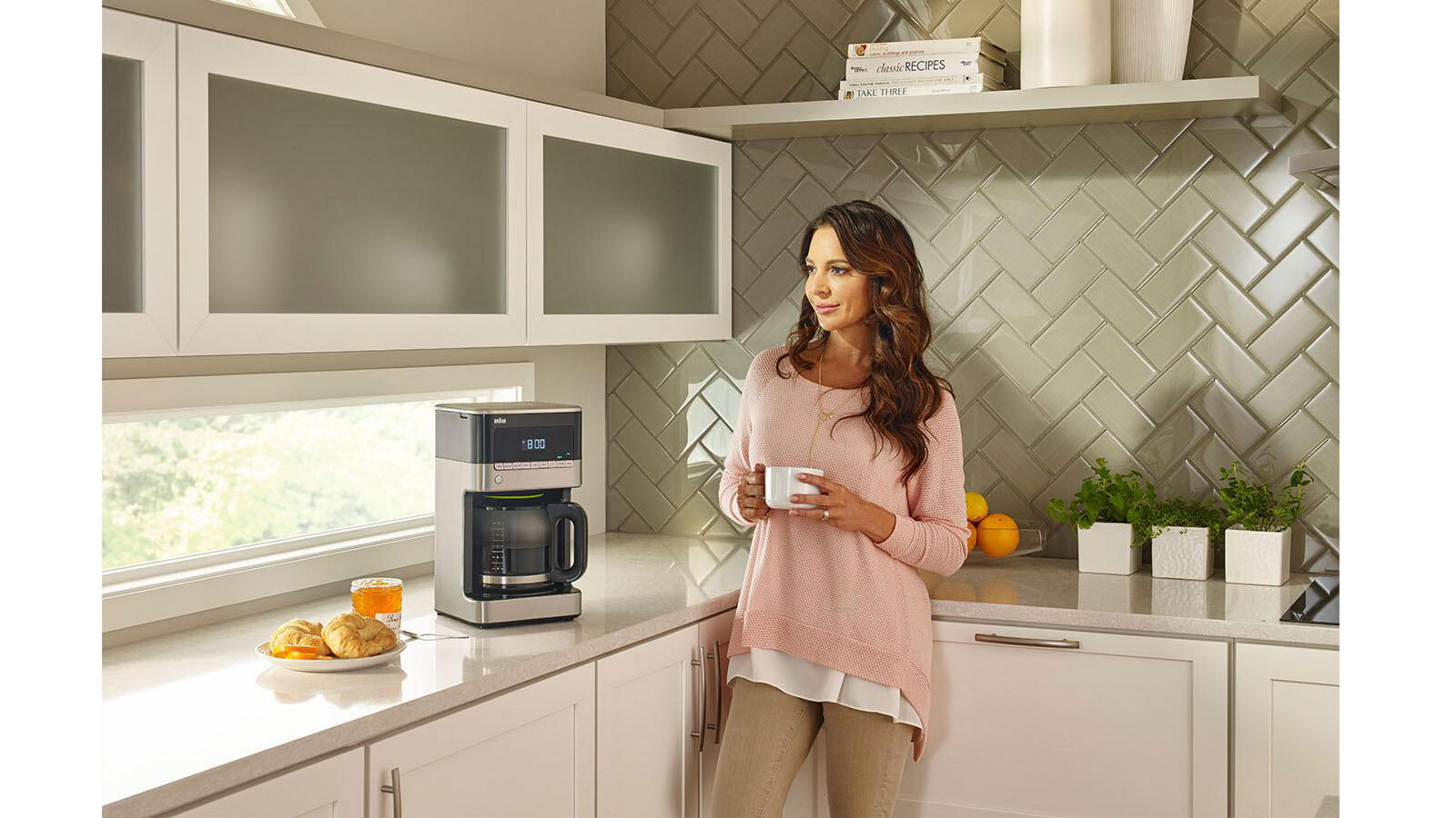 Kobieta w kuchni trzymająca filiżankę kawy, z ekspresem do kawy.