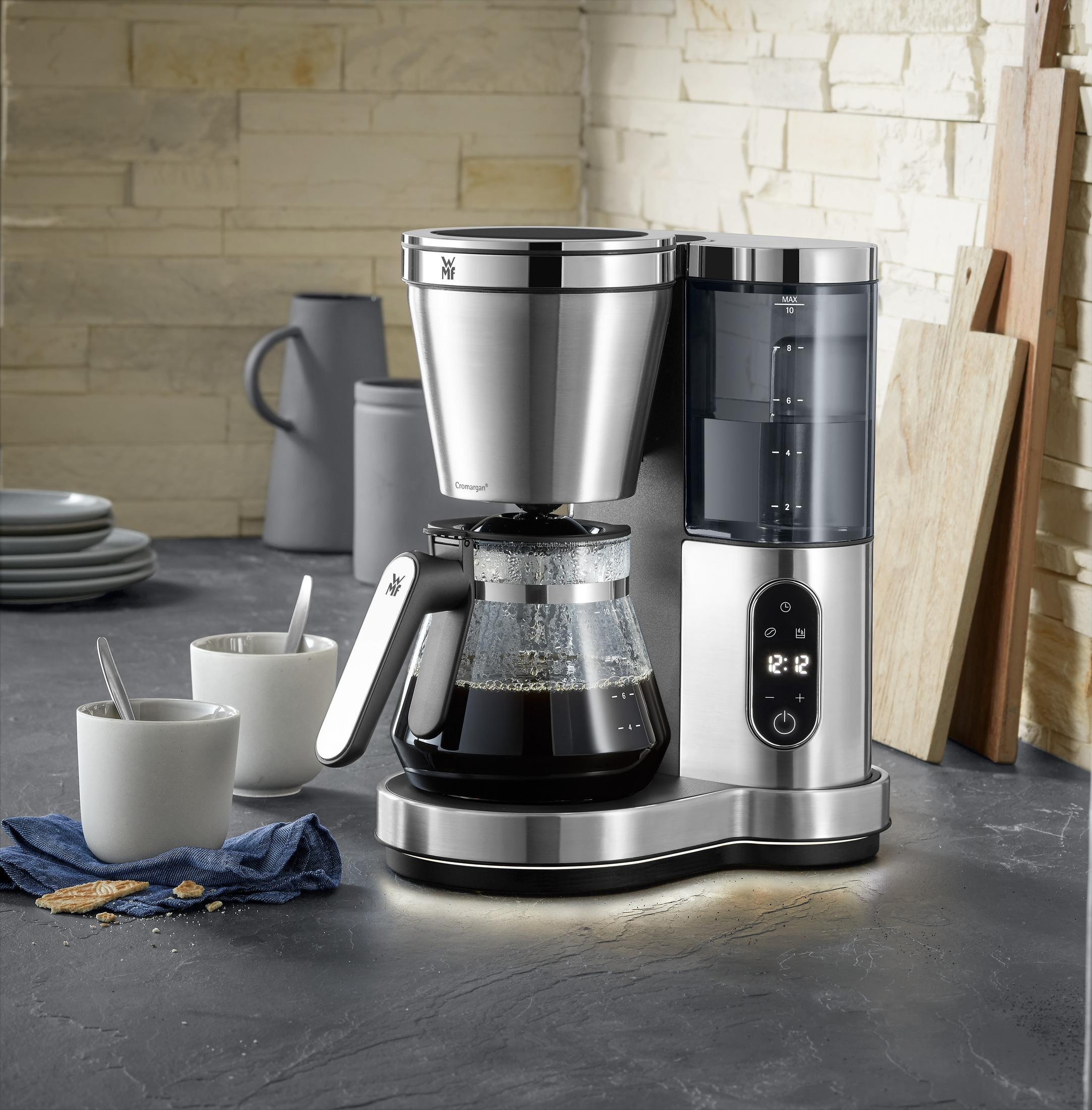 Ekspres do kawy ze stali nierdzewnej z karafką, filiżankami i drewnianymi deskami na blacie.