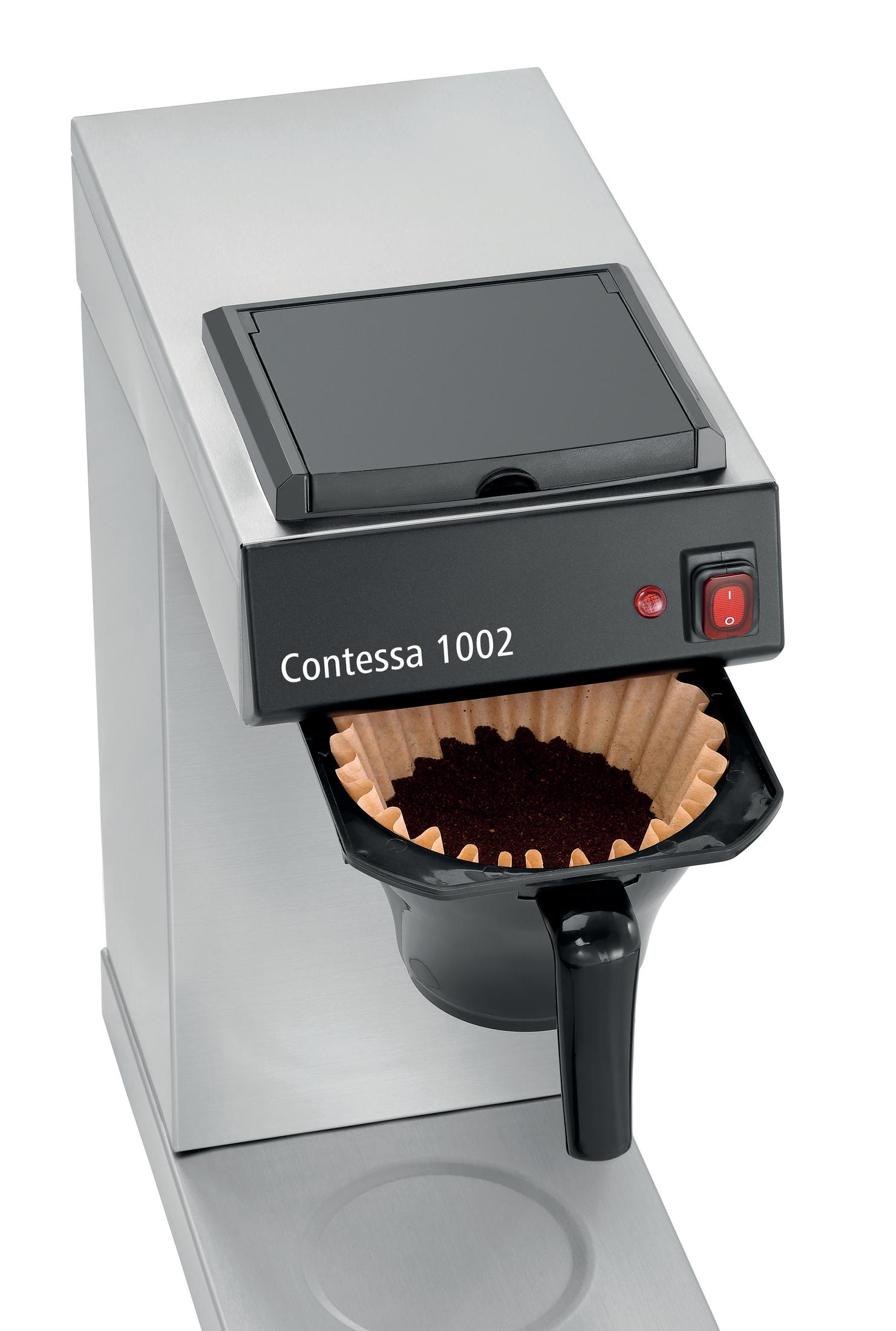 Cafetera con filtro de papel lleno de café molido. Acentos negros y un interruptor rojo.