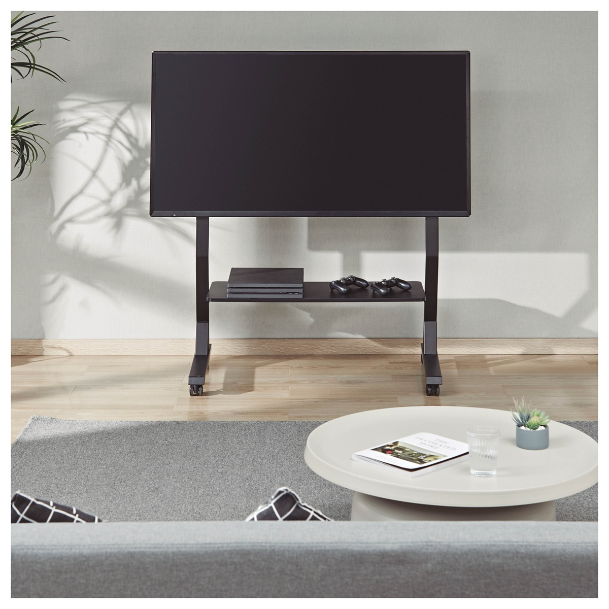 TV en un soporte negro con estante. Consola y mandos en el estante.