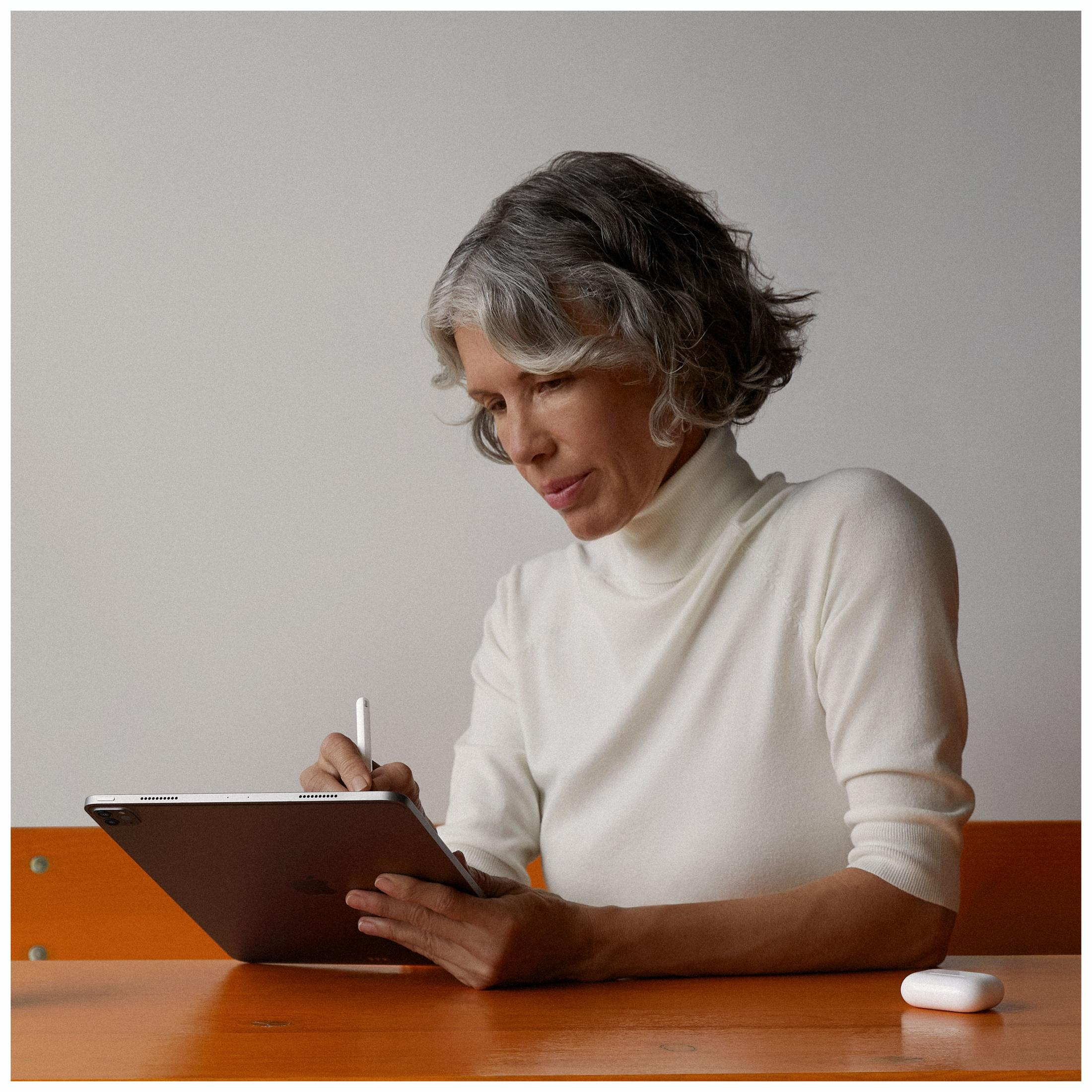 Kobieta używająca tabletu i rysika, z etui na airpody na pomarańczowym stole.