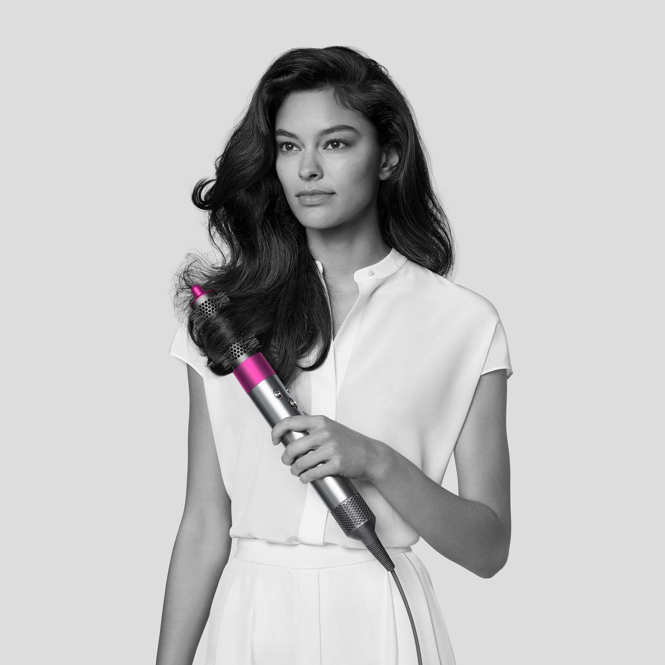Donna che tiene un arricciacapelli rosa e argento guardando di lato, in bianco e nero.