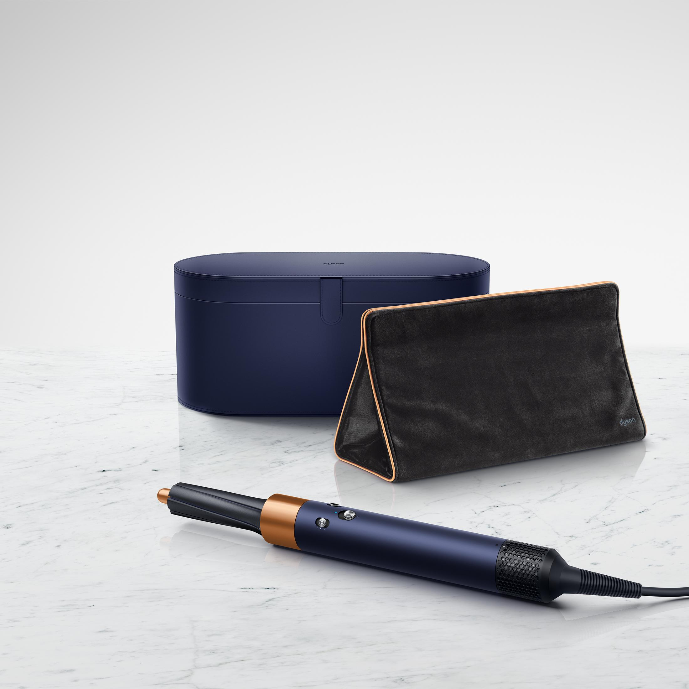 Un set di styling per capelli Dyson con custodia e borsa. Il set è su una superficie di marmo. Blu scuro e oro.
