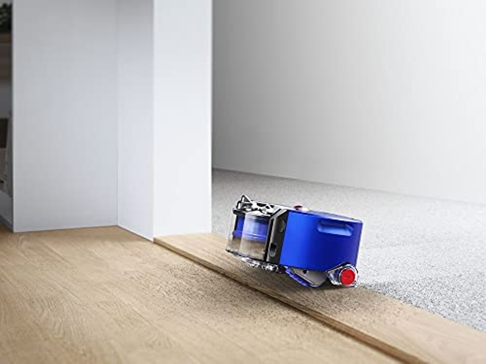 Ein blauer Roboter-Staubsauger auf Holz- und Teppichböden, in der Nähe einer weißen Wand.