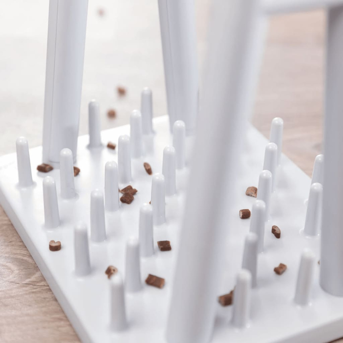 Biała miska dla zwierząt z kołkami i małymi kawałkami jedzenia. Jedzenie jest rozrzucone. Jasne tło.