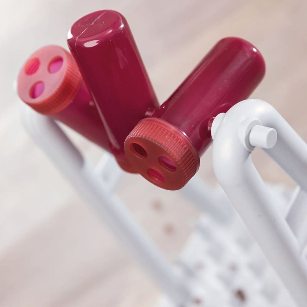 Trzy czerwone probówki z czerwonymi zakrętkami są umieszczone w białym stojaku. Probówki są do laboratorium.