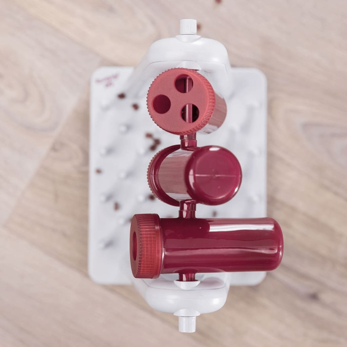 Zabawka dla psa z białą podstawą, czerwonymi elementami i tłem drewnianej podłogi.