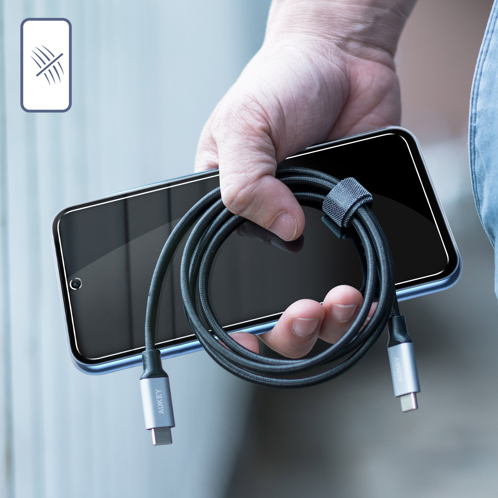 Mano sosteniendo cable USB-C negro junto a smartphone con protector de pantalla.