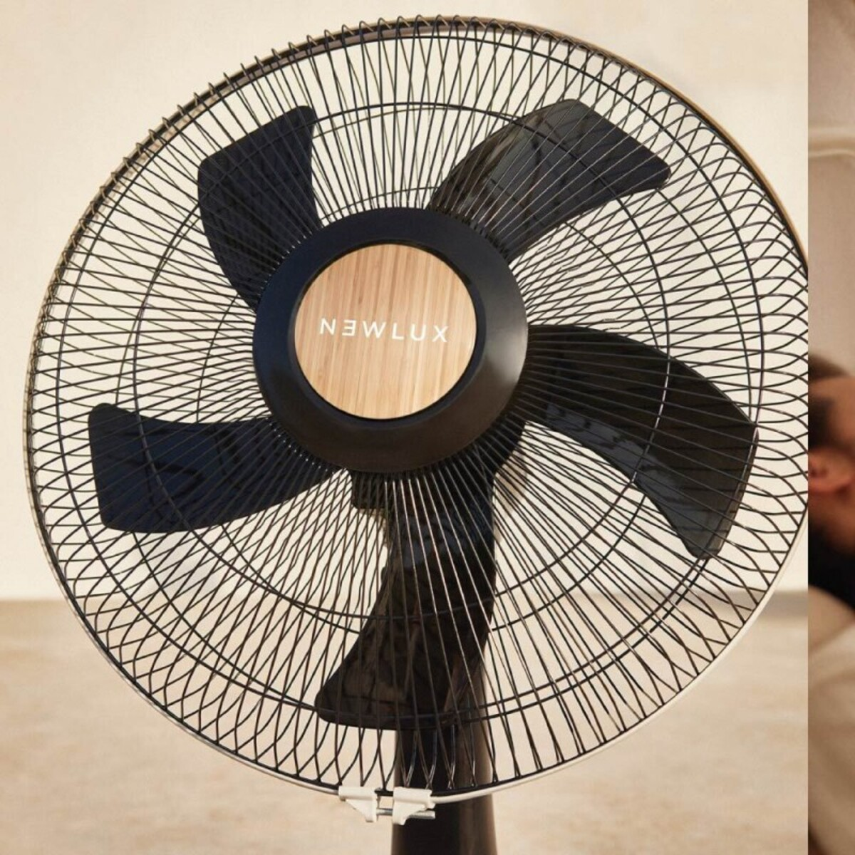 Ventilador negro y madera con rejilla protectora, persona en el fondo.