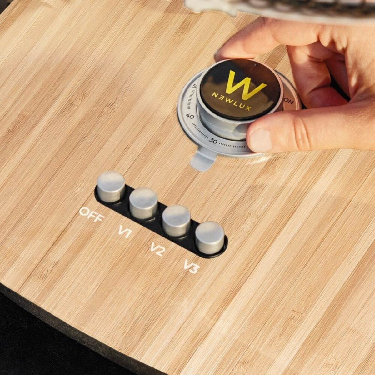 Mano girando dial en madera. Dial negro con logo Newlux y botones debajo.