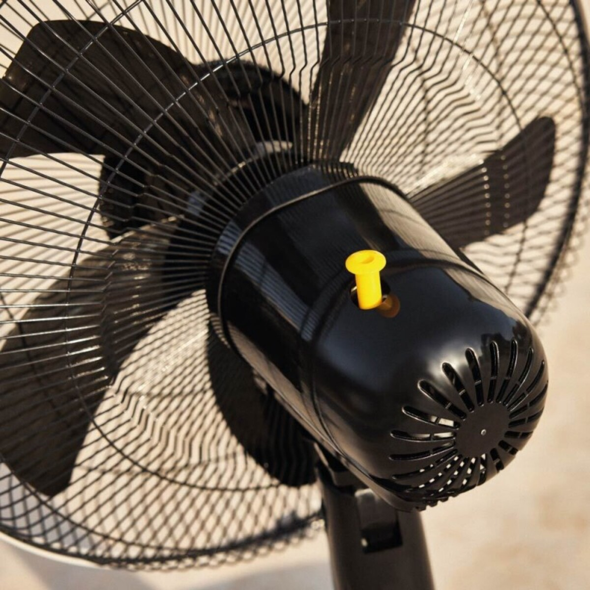 Primer plano de un ventilador negro con un botón amarillo y una malla metálica.