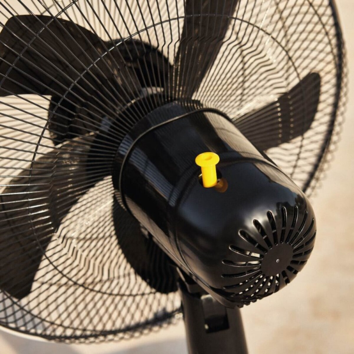 Primer plano de un ventilador negro con un botón amarillo en el centro y una base negra.