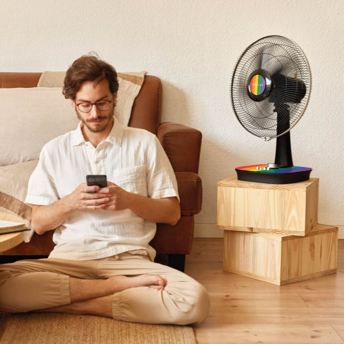 Hombre usando smartphone, sentado frente a ventilador sobre cajas de madera.