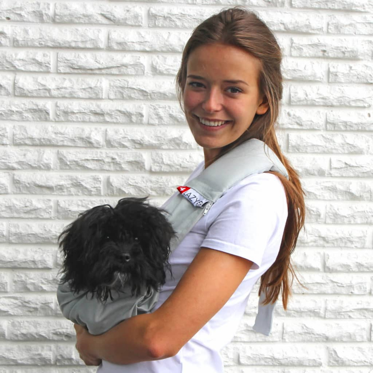 Une femme tenant un petit chien noir dans un sac de transport gris.