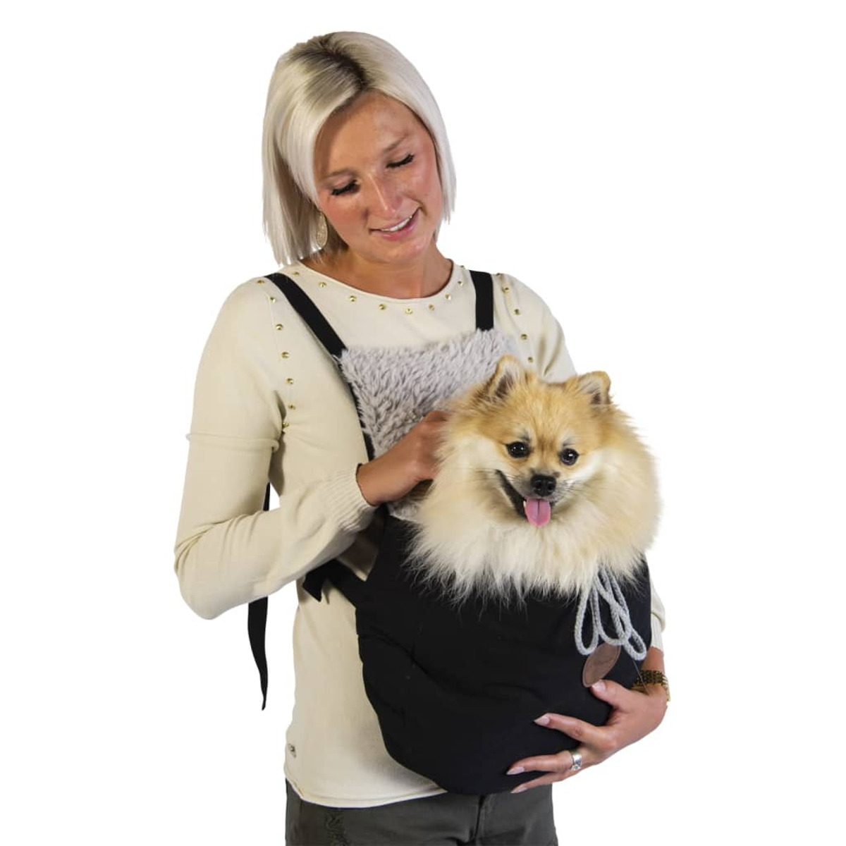 Eine Frau trägt einen kleinen Hund in einer Trage, der Hund ist blond und glücklich.