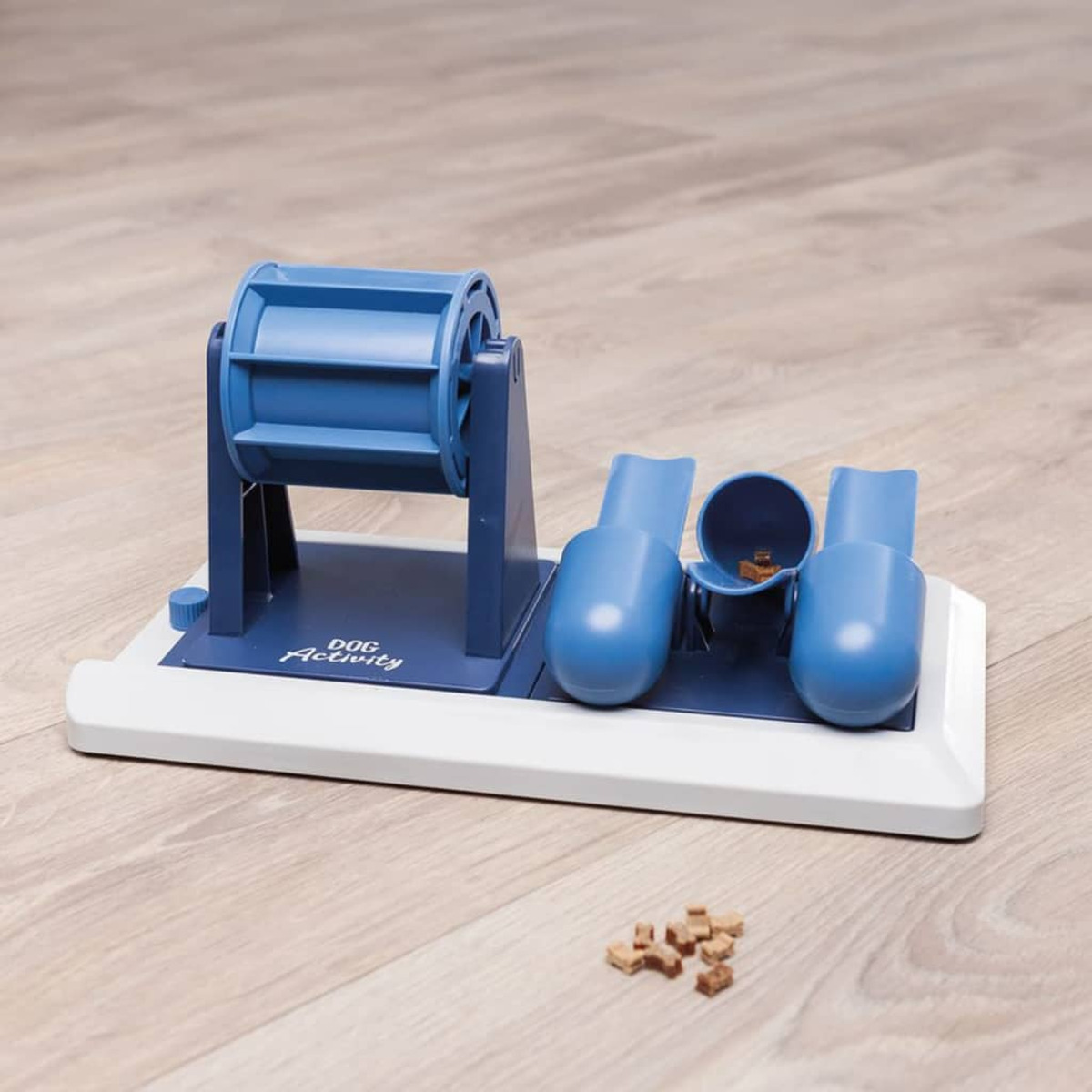 Un gioco per cani con un barilotto blu e due mestoli blu, su un pavimento in legno chiaro.