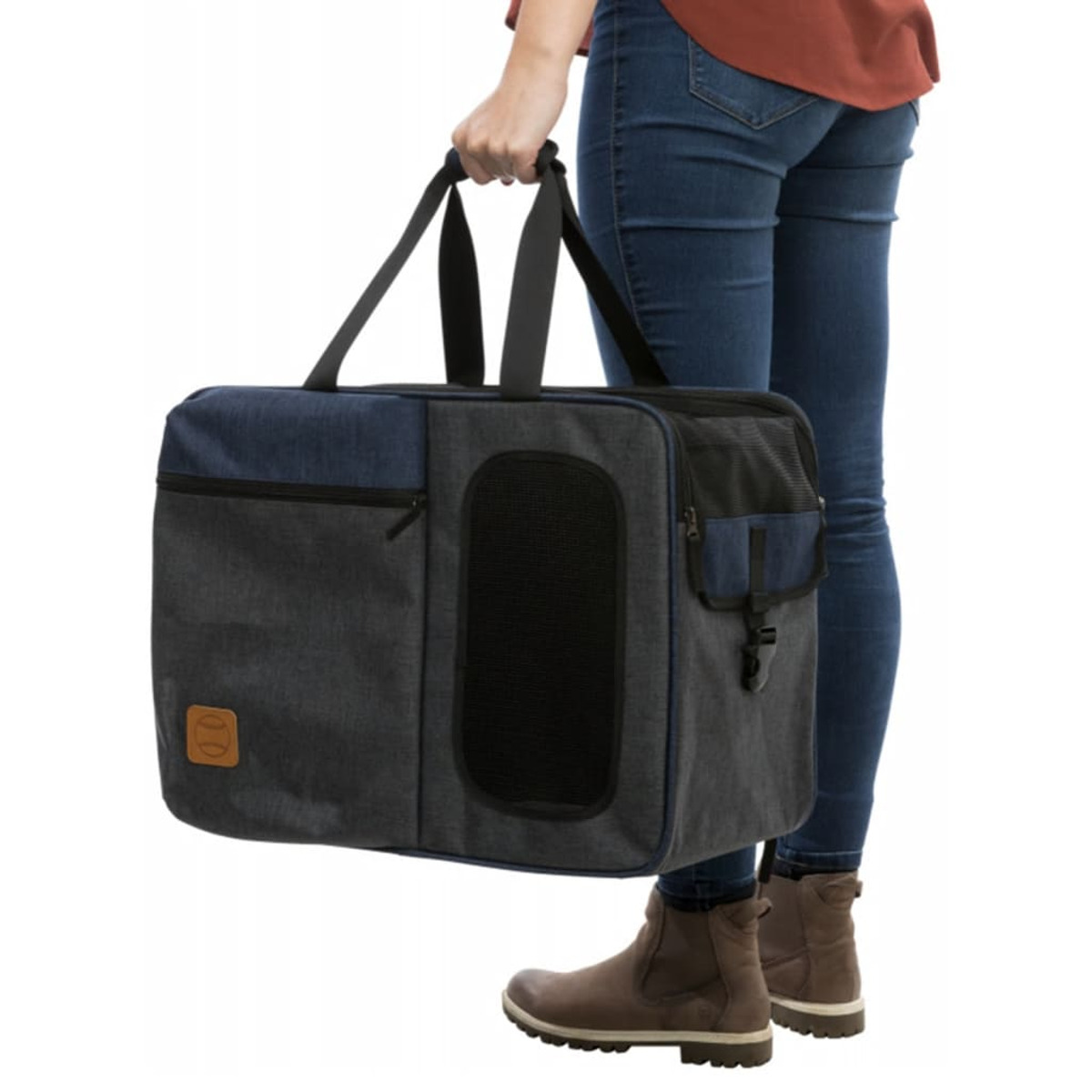 Person, die eine Haustiertasche hält. Die Tasche ist blau und grau. Die Person trägt Jeans und braune Stiefel.