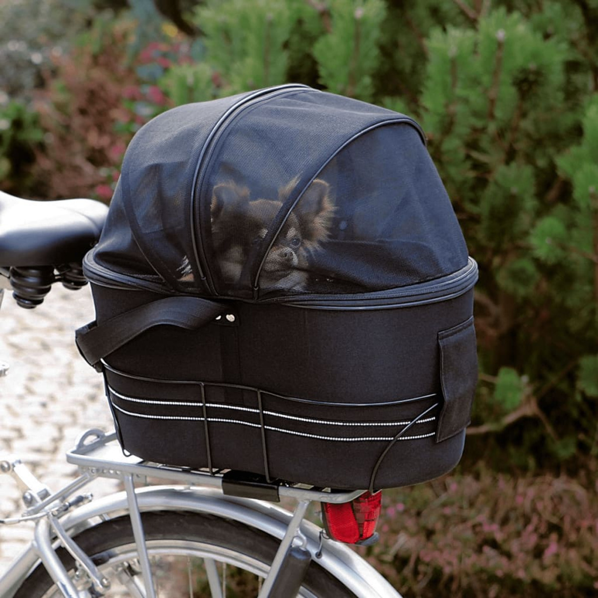 Ein Hund in einem schwarzen Fahrradkorb mit Netzabdeckung, an einem Fahrrad befestigt.