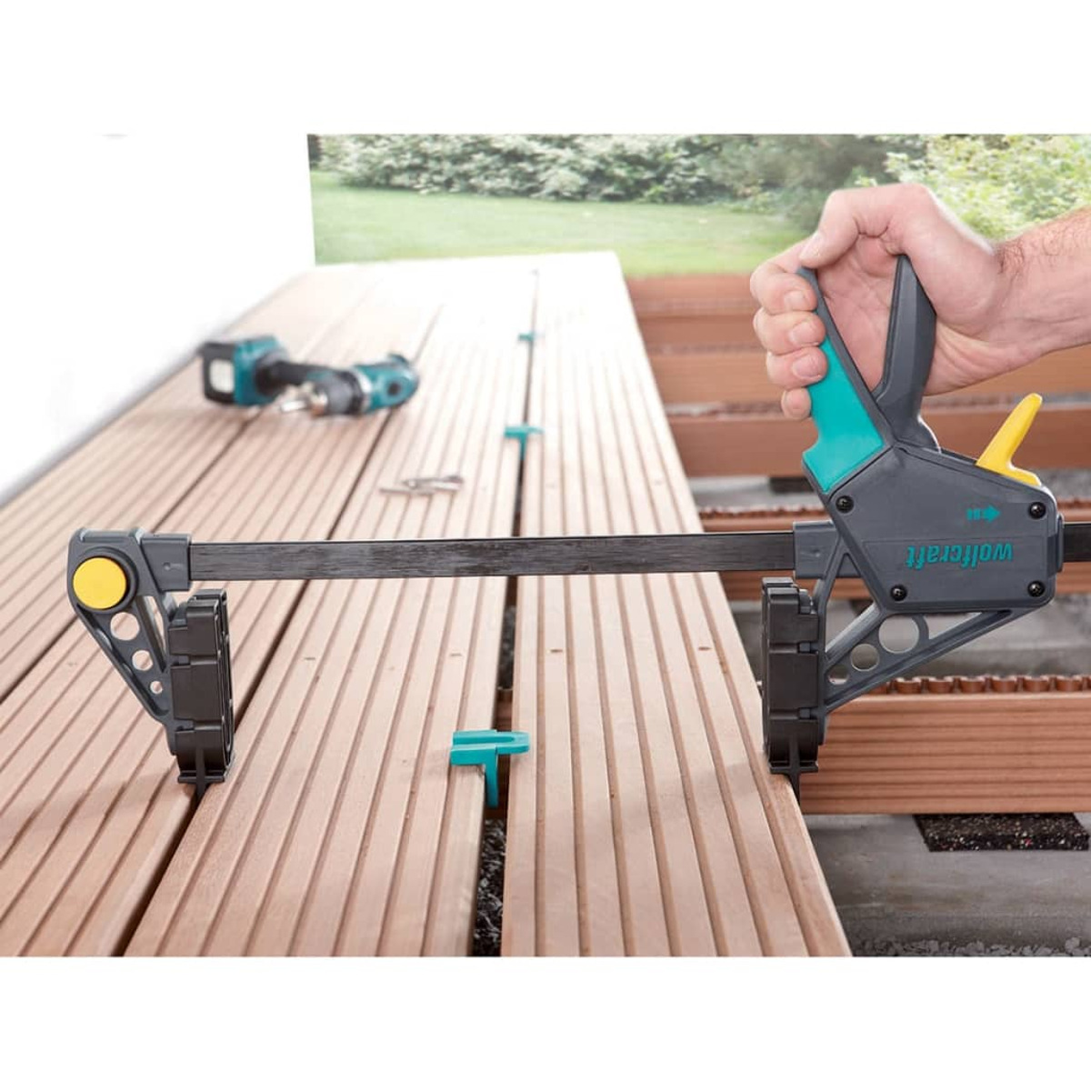 Mano che tiene un morsetto. Terrazza in legno sullo sfondo.
