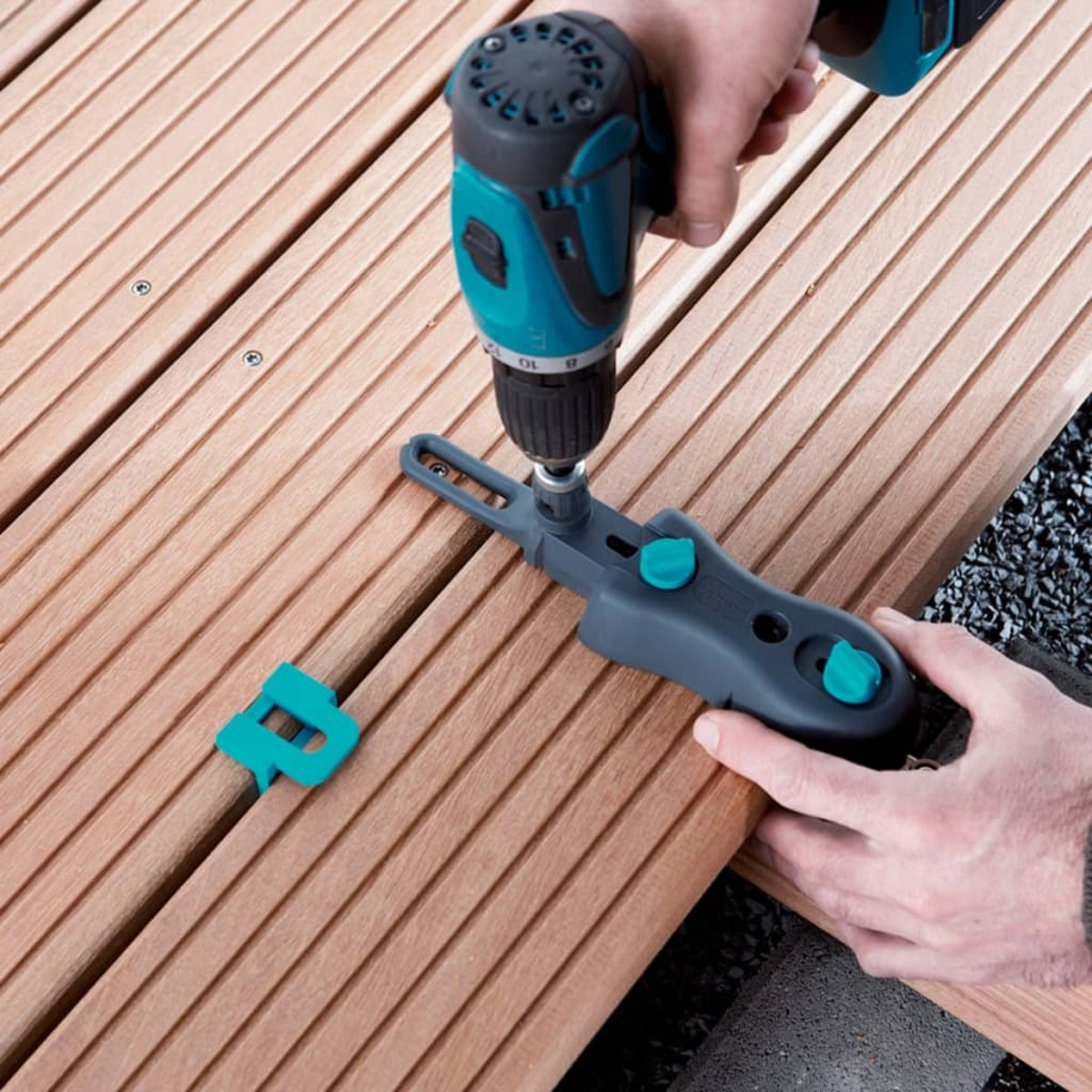 Una persona usa un trapano per installare una clip per decking su assi di legno. È visibile anche un attrezzo.