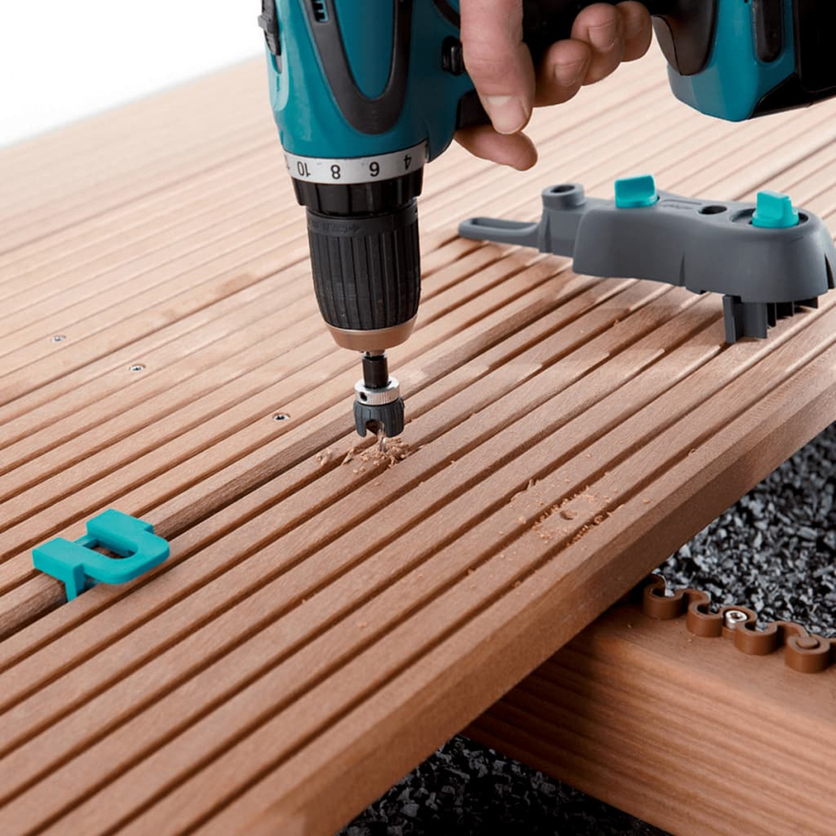 Un trapano sta forando una tavola di legno. Un pezzo di plastica blu a sinistra.
