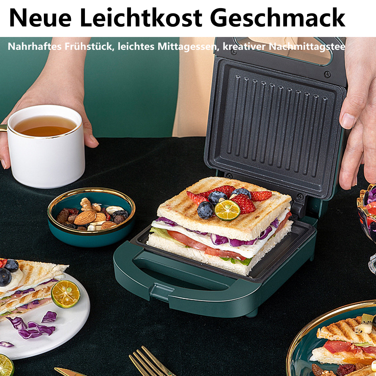 Sandwichmaker mit aufgeschnittenem Sandwich, Tee, Nüssen und Früchten auf einem Tisch.