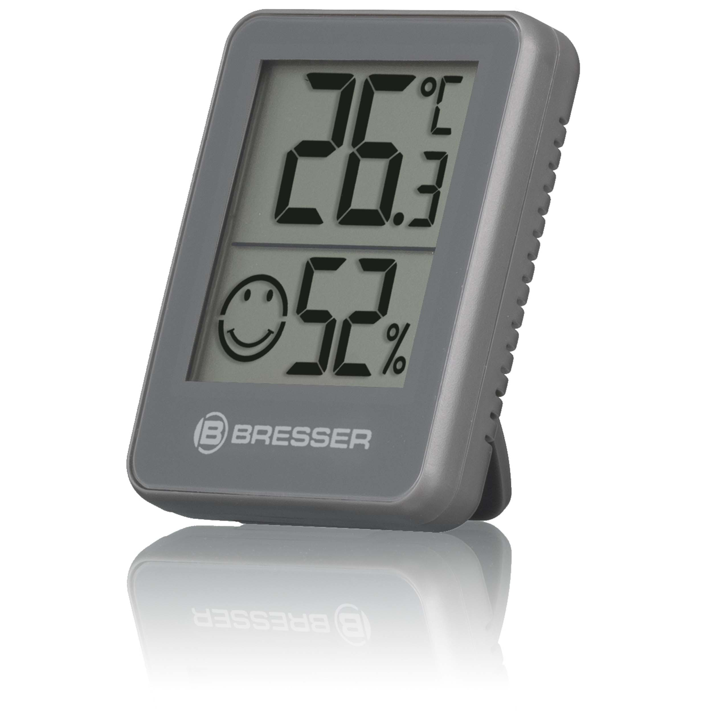 Ein graues digitales Thermometer, das Temperatur und Luftfeuchtigkeit mit einem lächelnden Gesicht anzeigt.