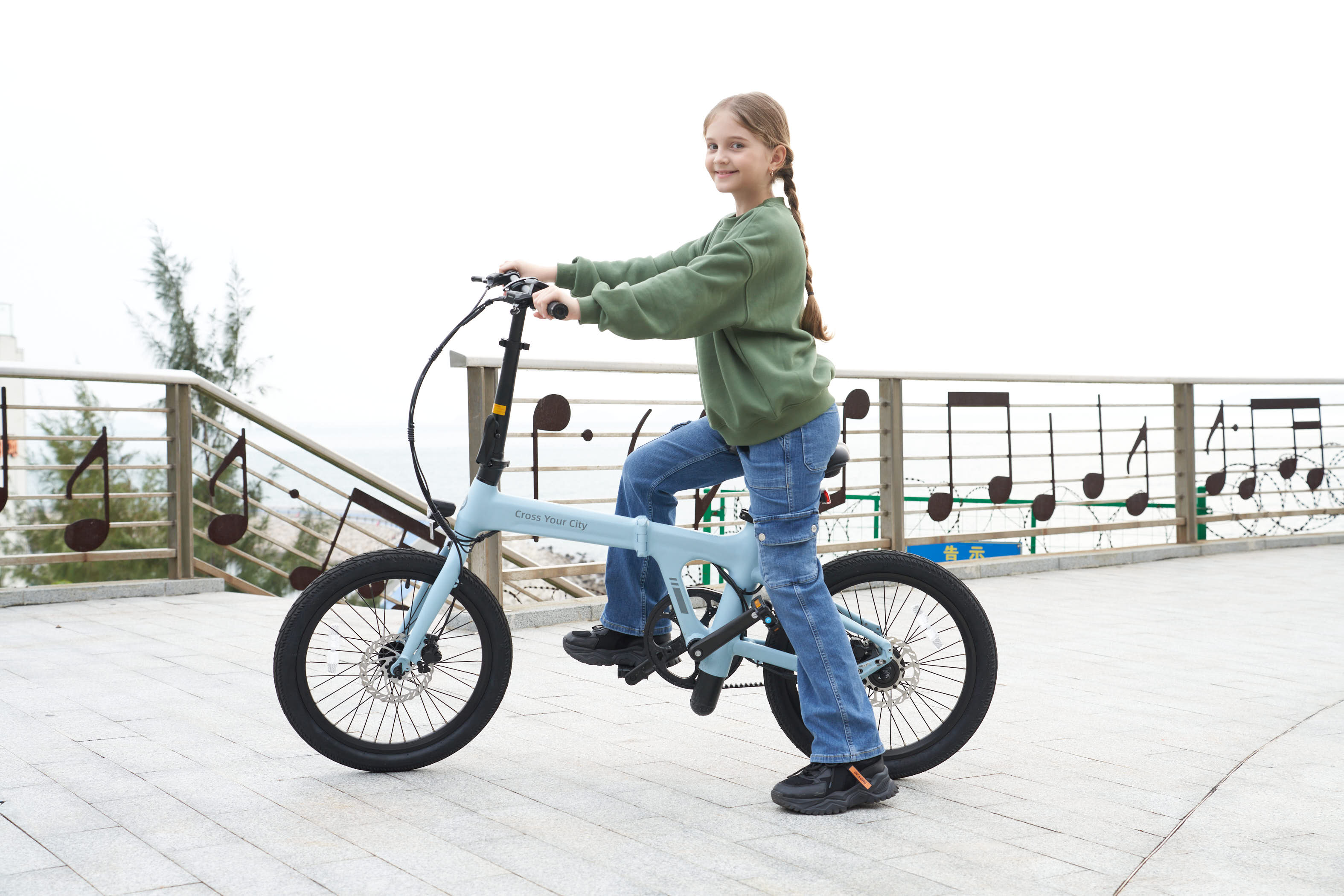 Dziewczyna na niebieskim składanym rowerze uśmiecha się do kamery na ścieżce z barierką z nutami.