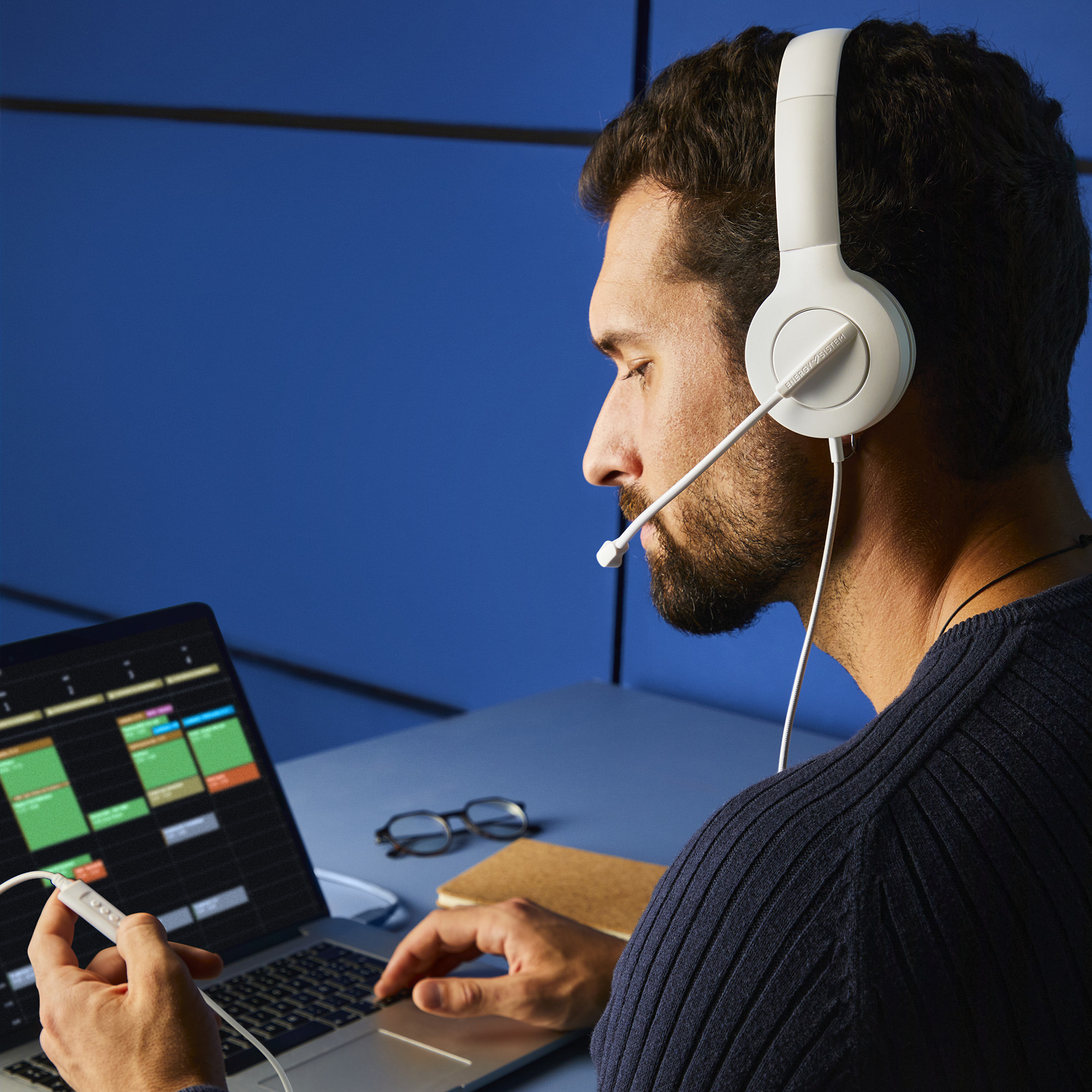 Hombre con auriculares blancos trabajando en un portátil con aplicación de calendario abierta.