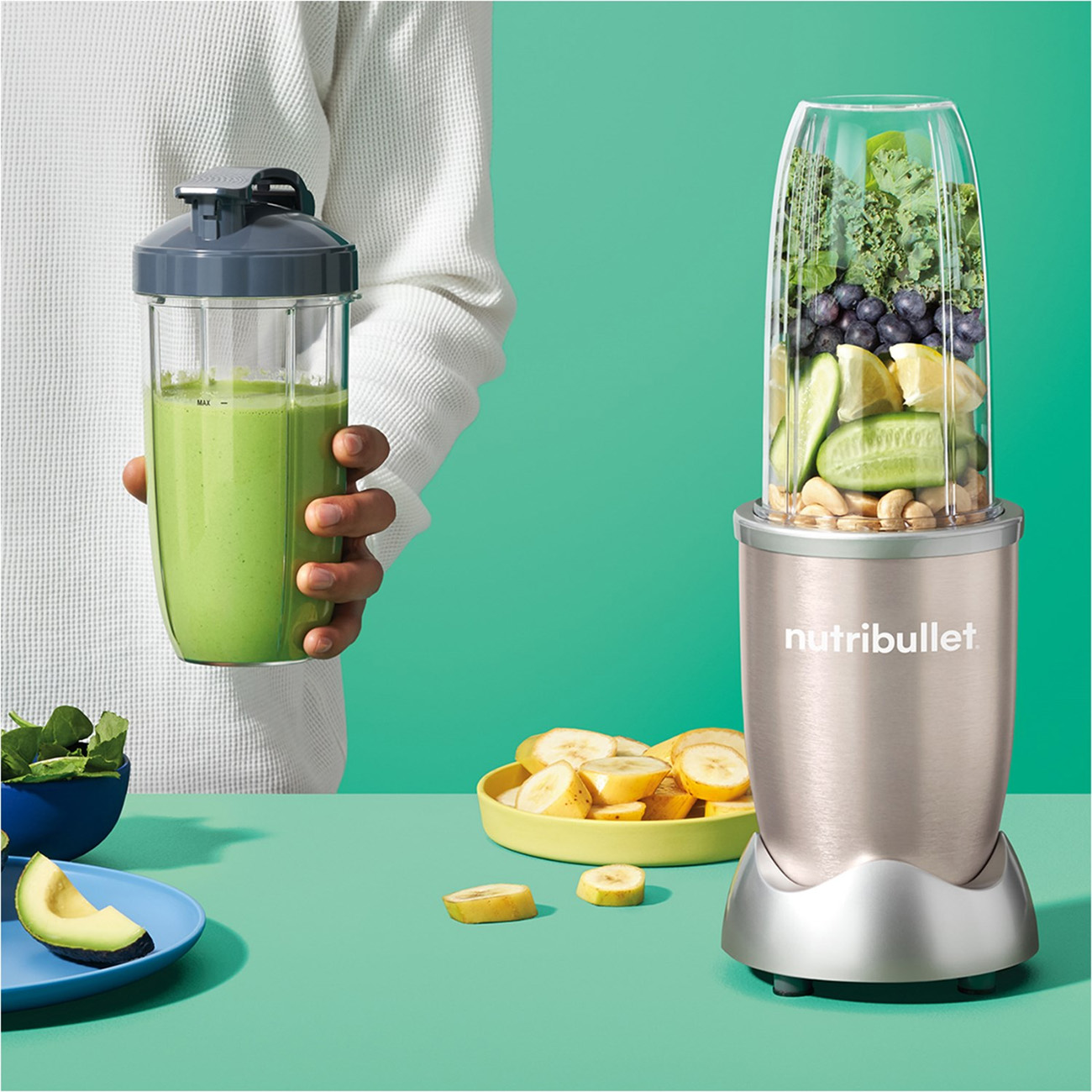 Eine Person hält einen grünen Smoothie und einen Nutribullet. Verschiedene Zutaten sind im Mixer.