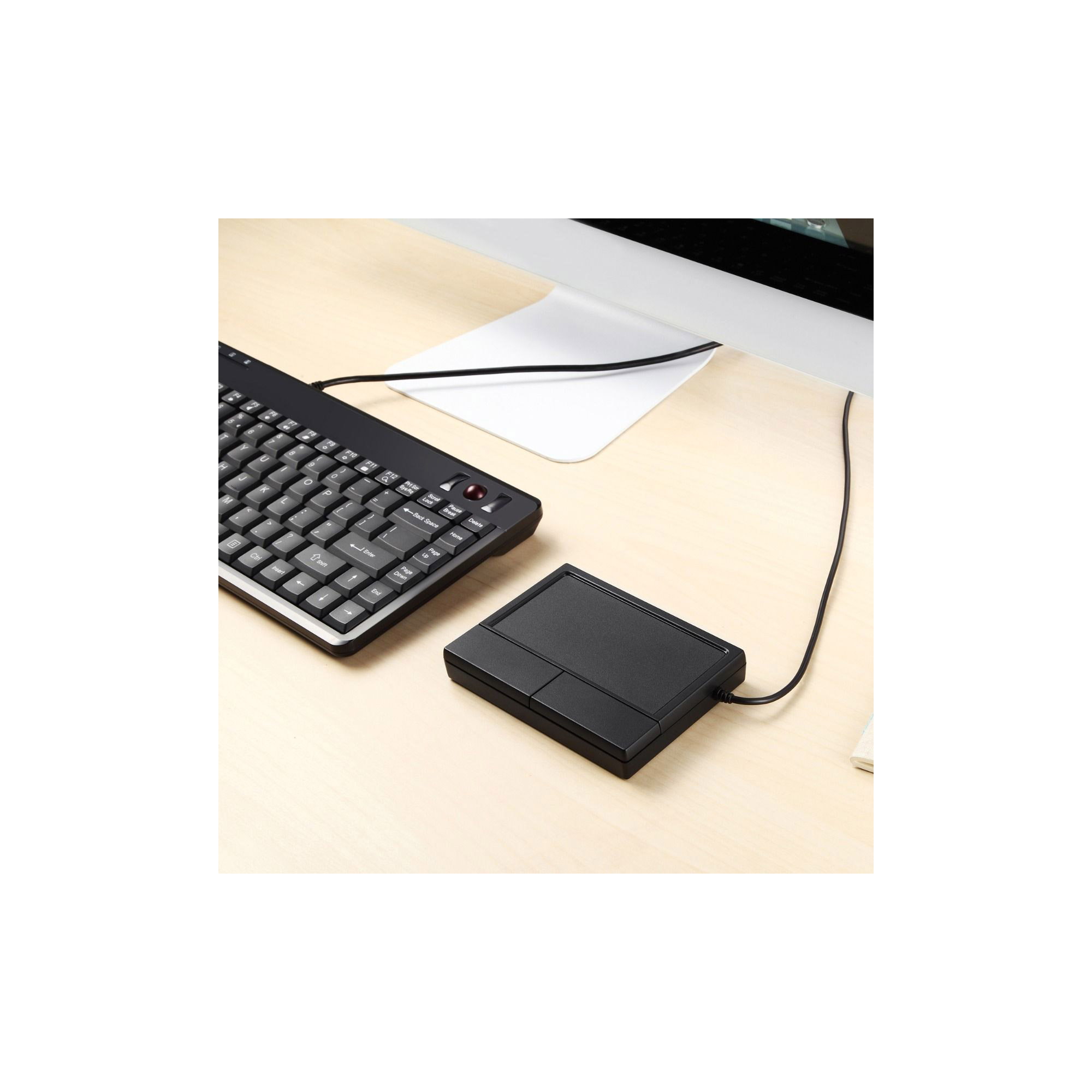 Schwarze Tastatur und Touchpad auf einem Holztisch, mit einem weißen Computermonitor im Hintergrund.