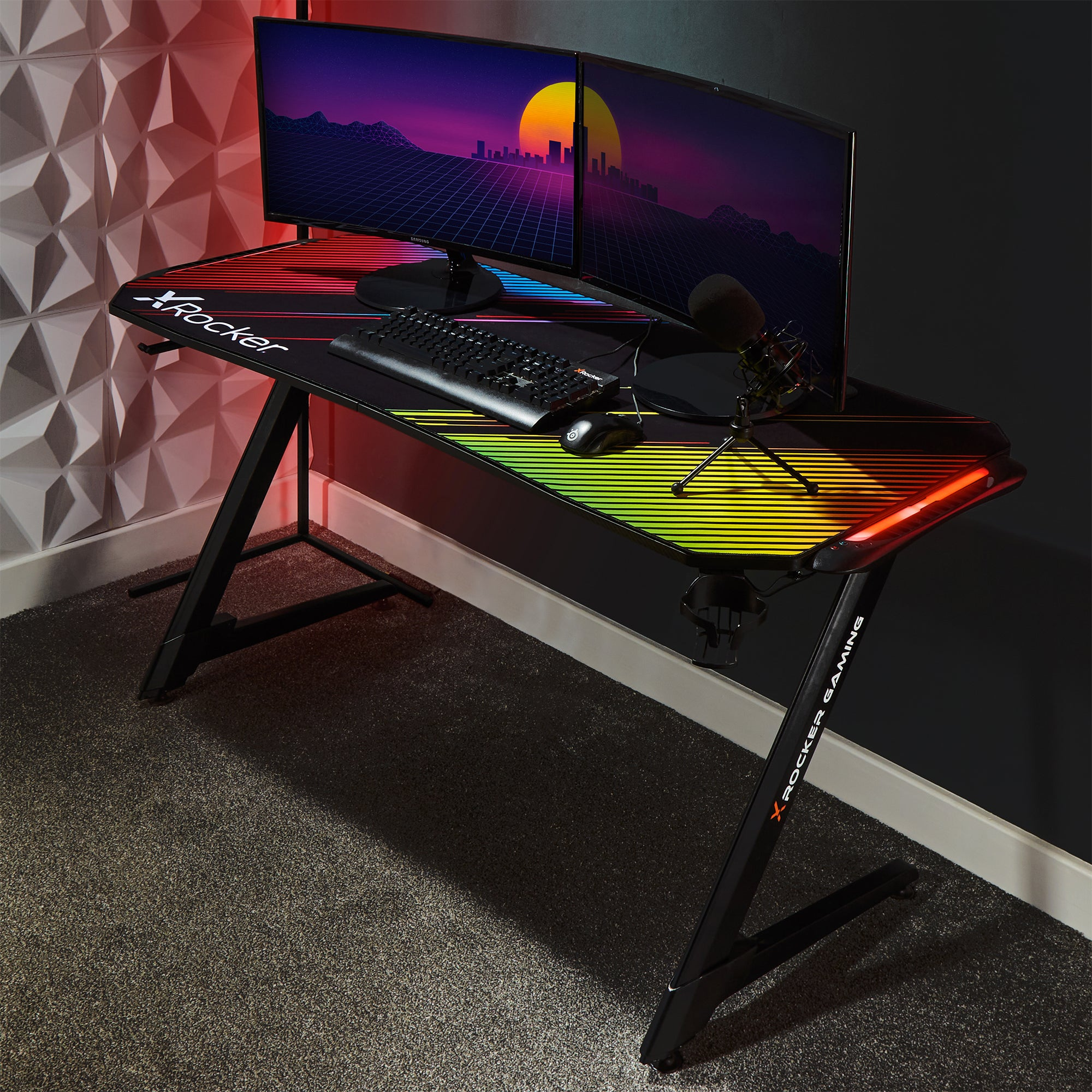 Gaming-Schreibtisch mit schwarzer Oberfläche, zwei Monitoren, Tastatur, Maus und Mikrofon.
