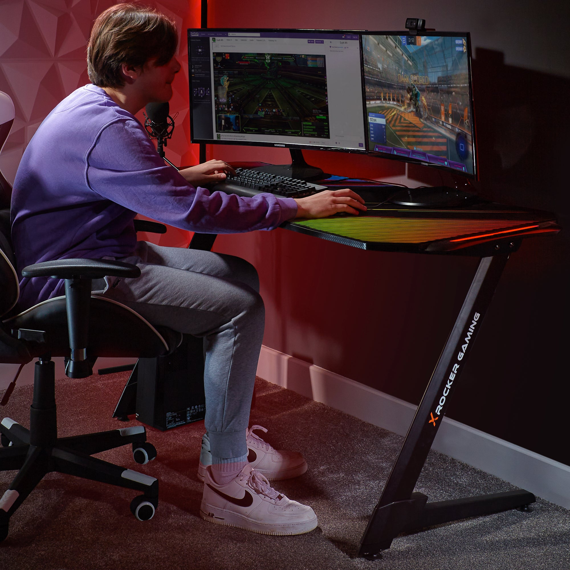 Gamer am Schreibtisch, Monitor zeigt Gameplay, mit Mikrofon, Tastatur und Stuhl. Der Tisch hat RGB-Beleuchtung.