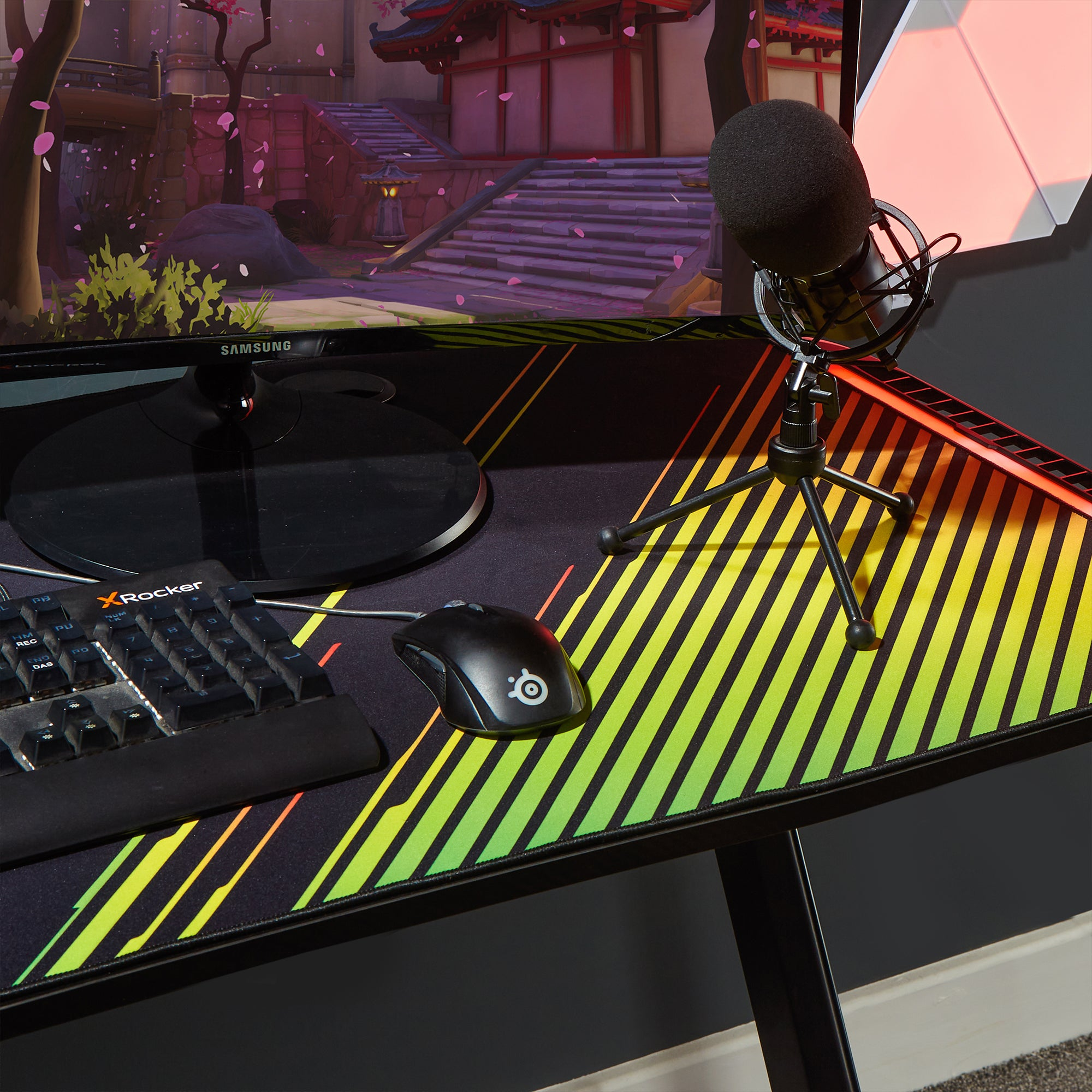 Gaming-Setup: Tastatur, Maus und Monitor, der ein Spiel anzeigt. Mikrofon auf Ständer.