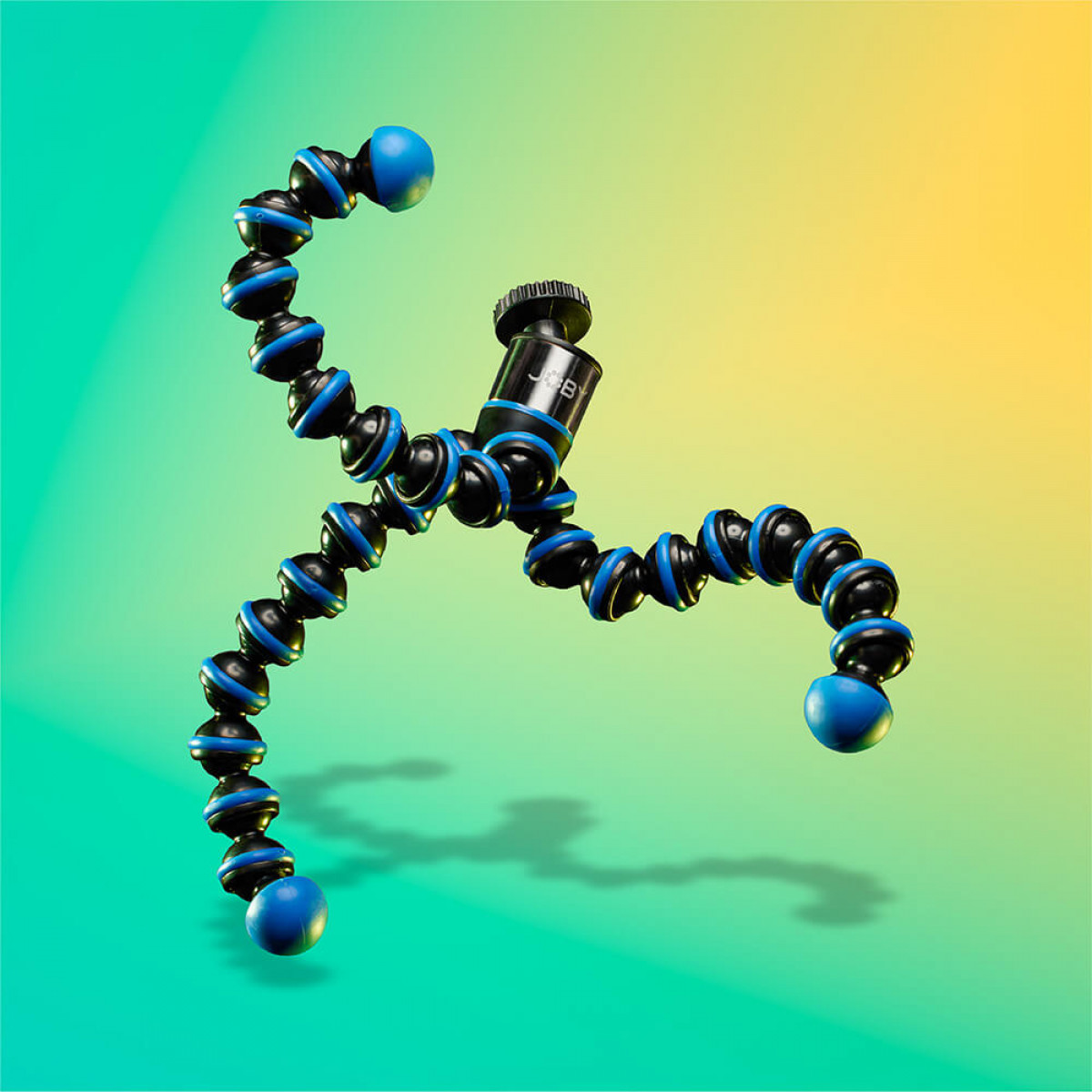 Ein schwarzes, flexibles Stativ mit blauen Gelenken. Es ist vor einem farbigen Hintergrund aus Gelb und Grün platziert.