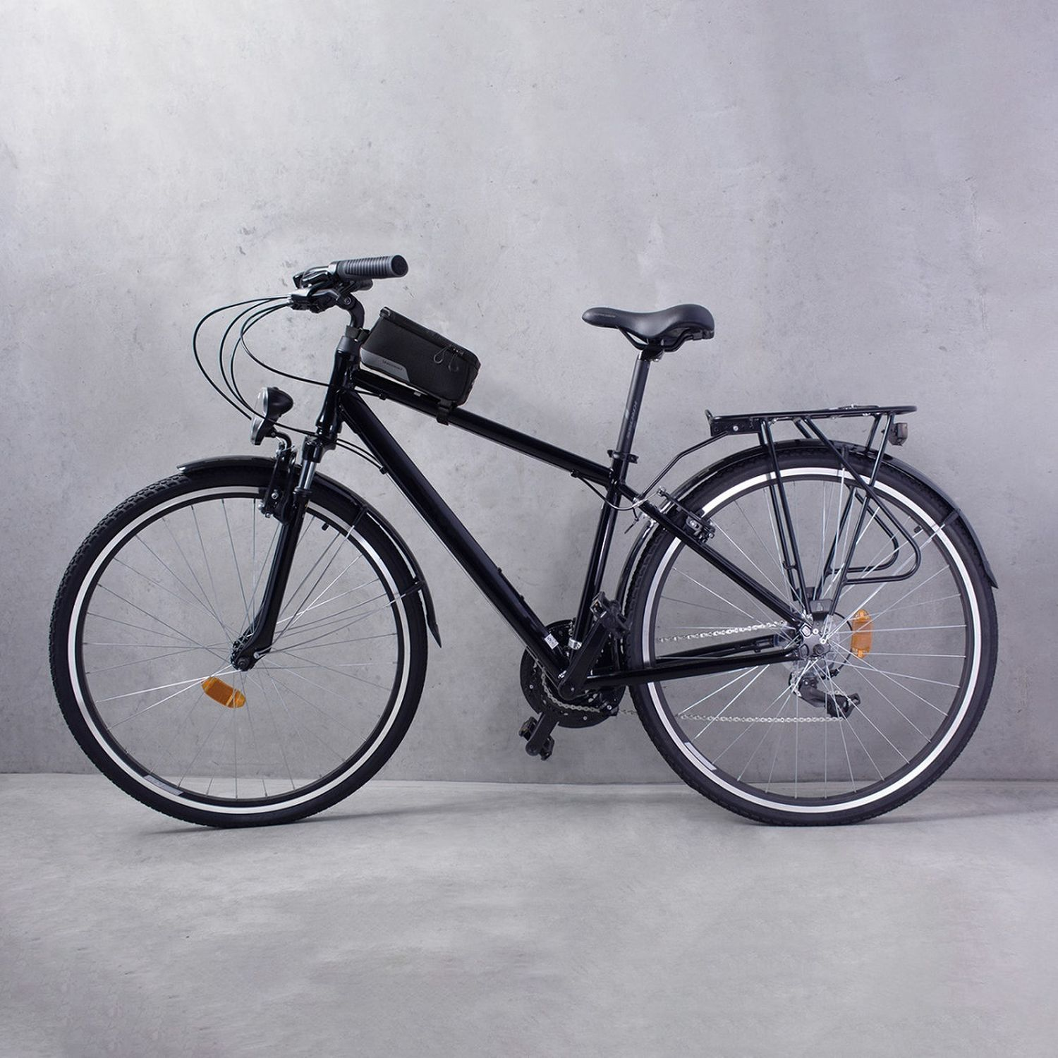 Schwarzes Fahrrad mit schwarzem Rahmen und schwarzer Gepäcktasche vor grauer Wand.