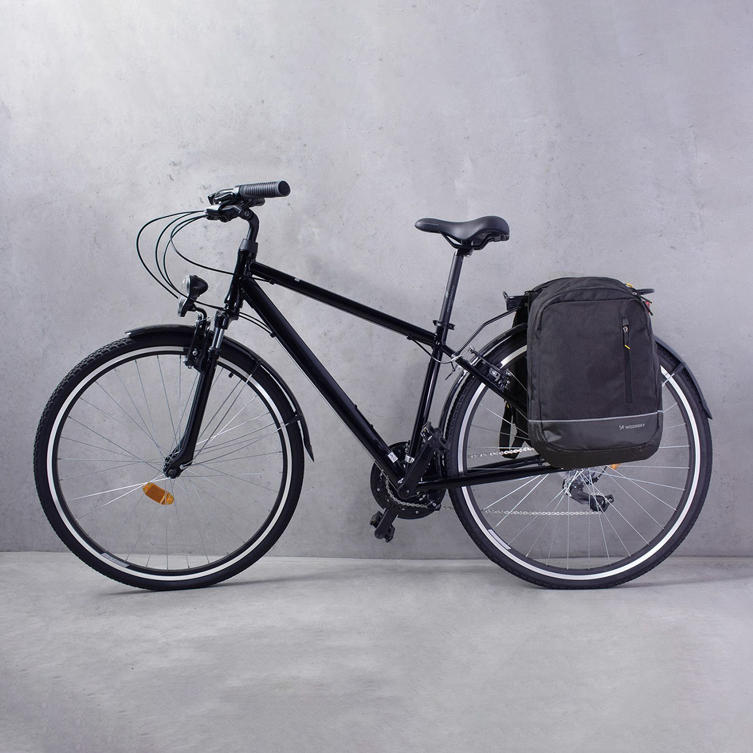 Schwarzes Fahrrad mit schwarzer Tasche hinten, vor grauer Wand.